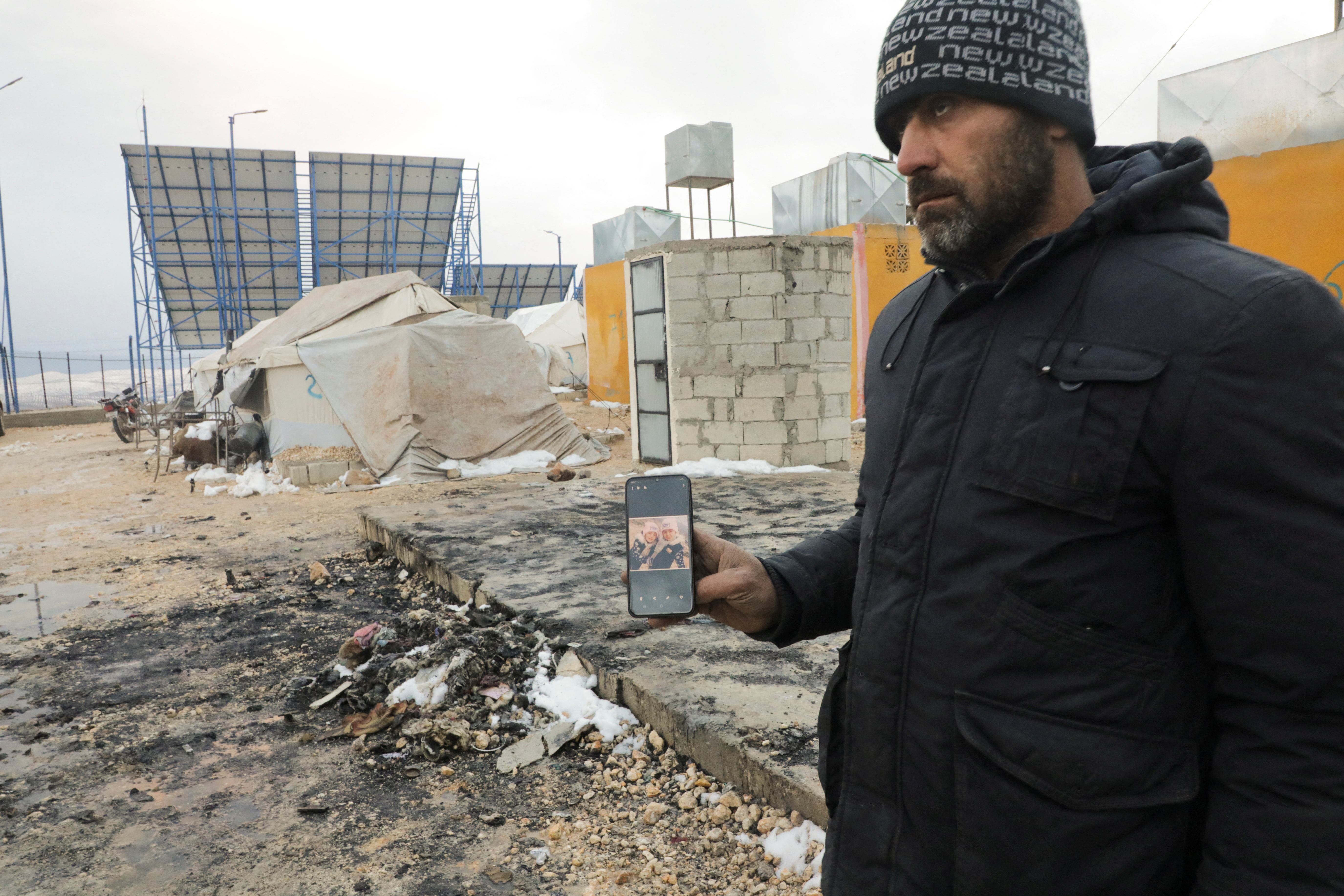 Nouredin al-Abdullah holds a mobile phone with pictures of Lin and Intissar displayed on a mobile screen at a camp for the internally displaced in the countryside in Aleppo