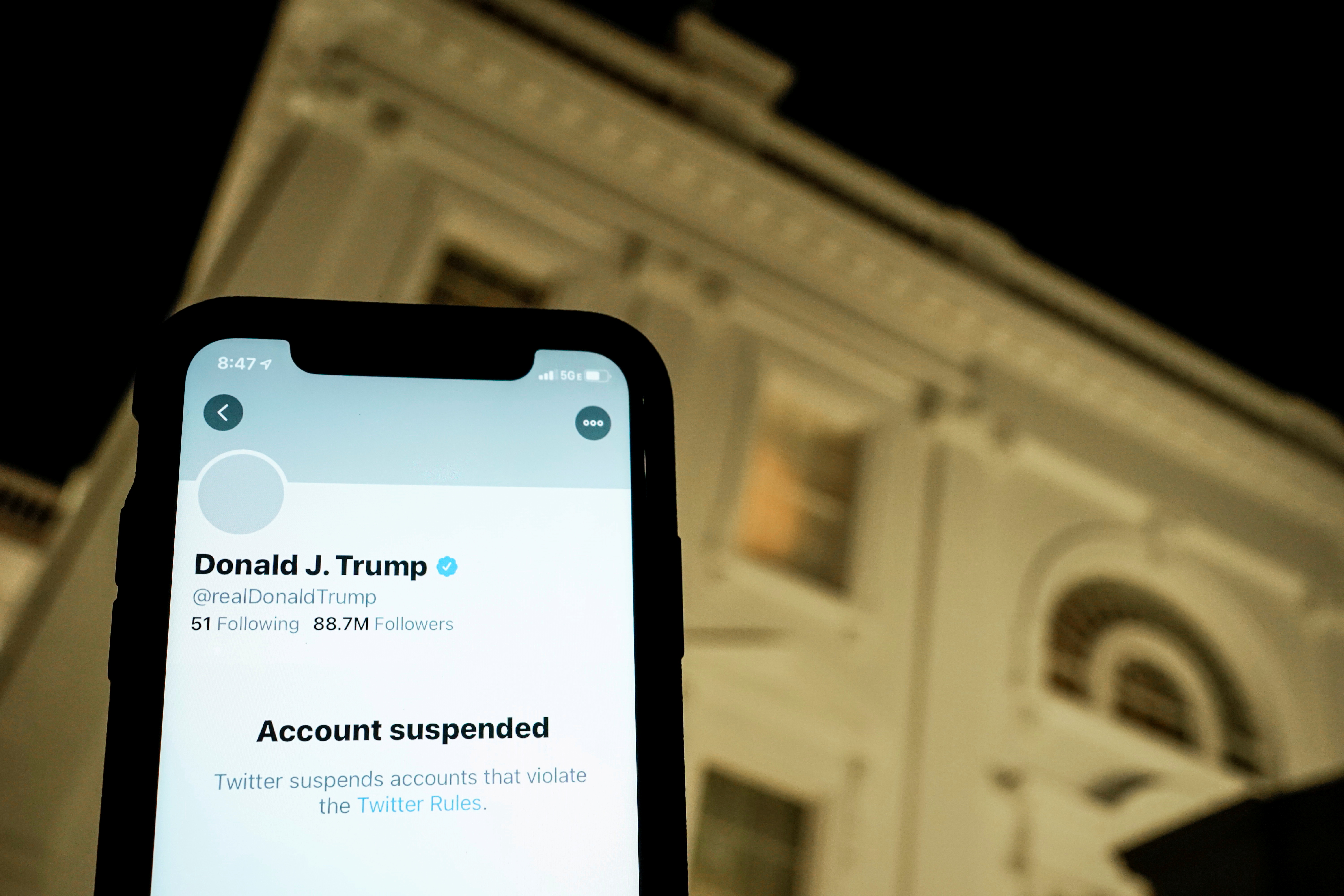 A photo illustration shows the suspended Twitter account of U.S. President Donald Trump on a smartphone and a lit window in the White House residence in Washington