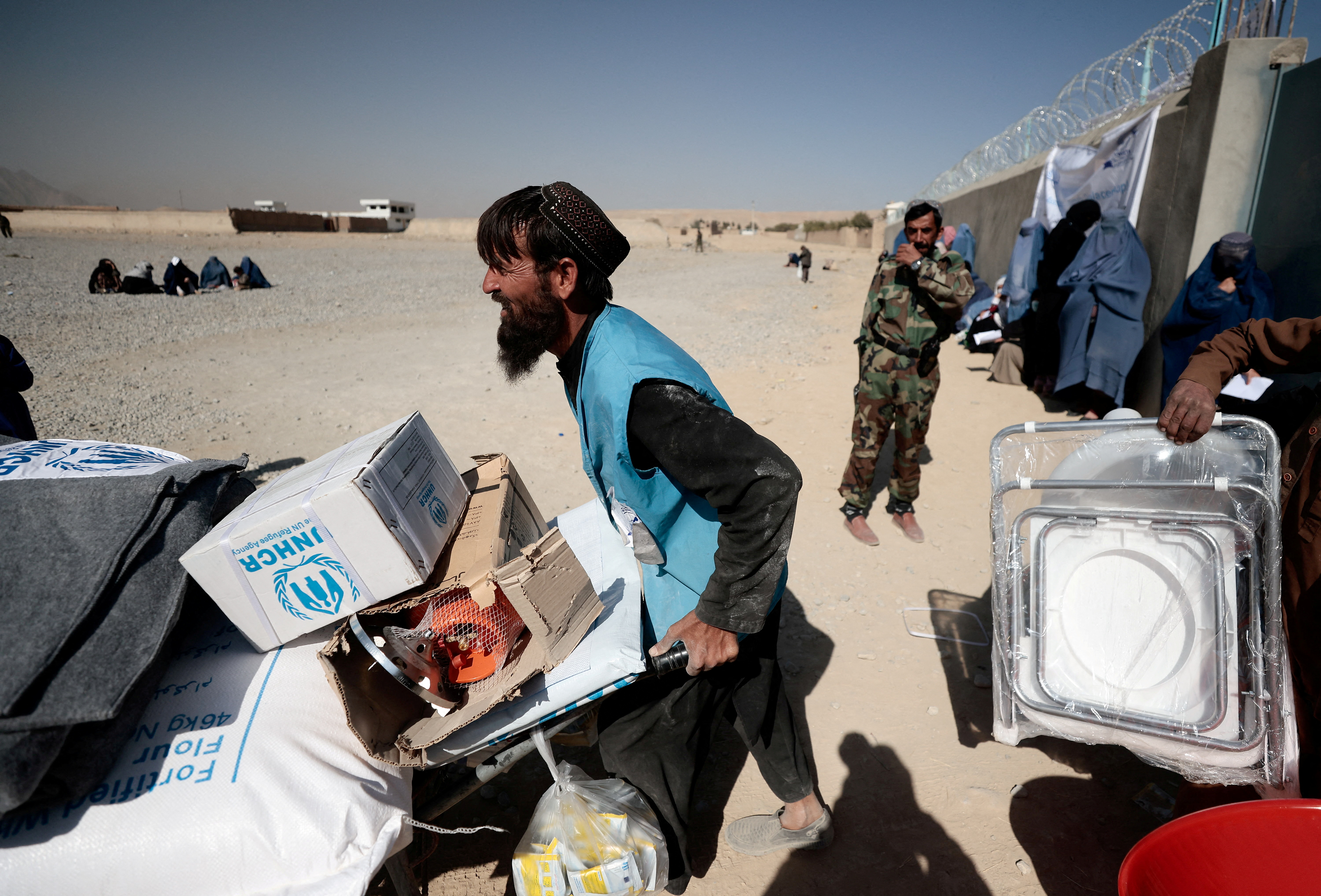 UNHCR worker pushes a wheelbarrow loaded with aid supplies for a displaced Afghan family outside a distribution center on the outskirts of Kabul