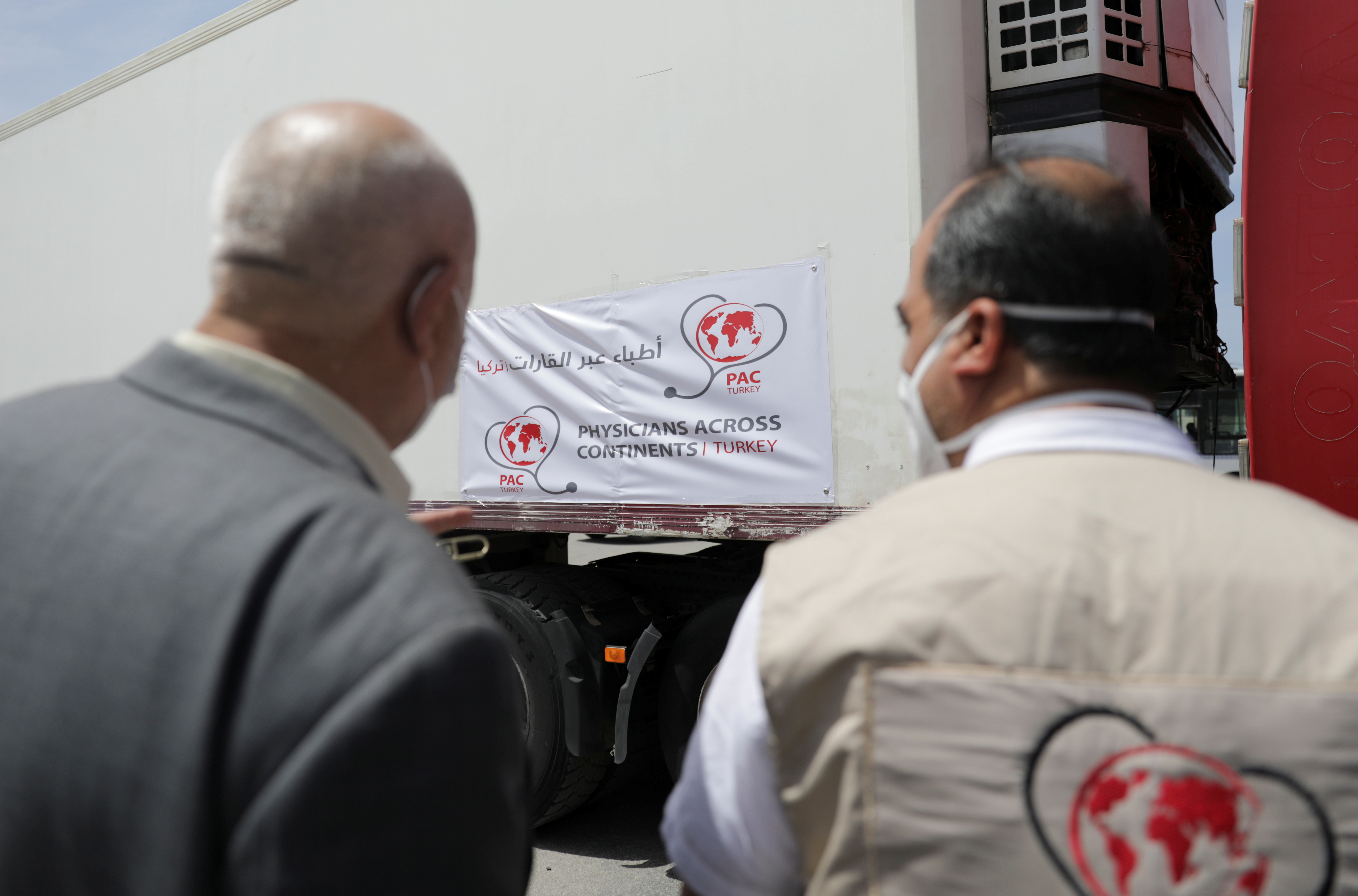 Healthcare workers stand near a truck carrying vaccines against the coronavirus disease (COVID-19) at Bab al-Hawa crossing at the Syrian-Turkish border, in Idlib governorate