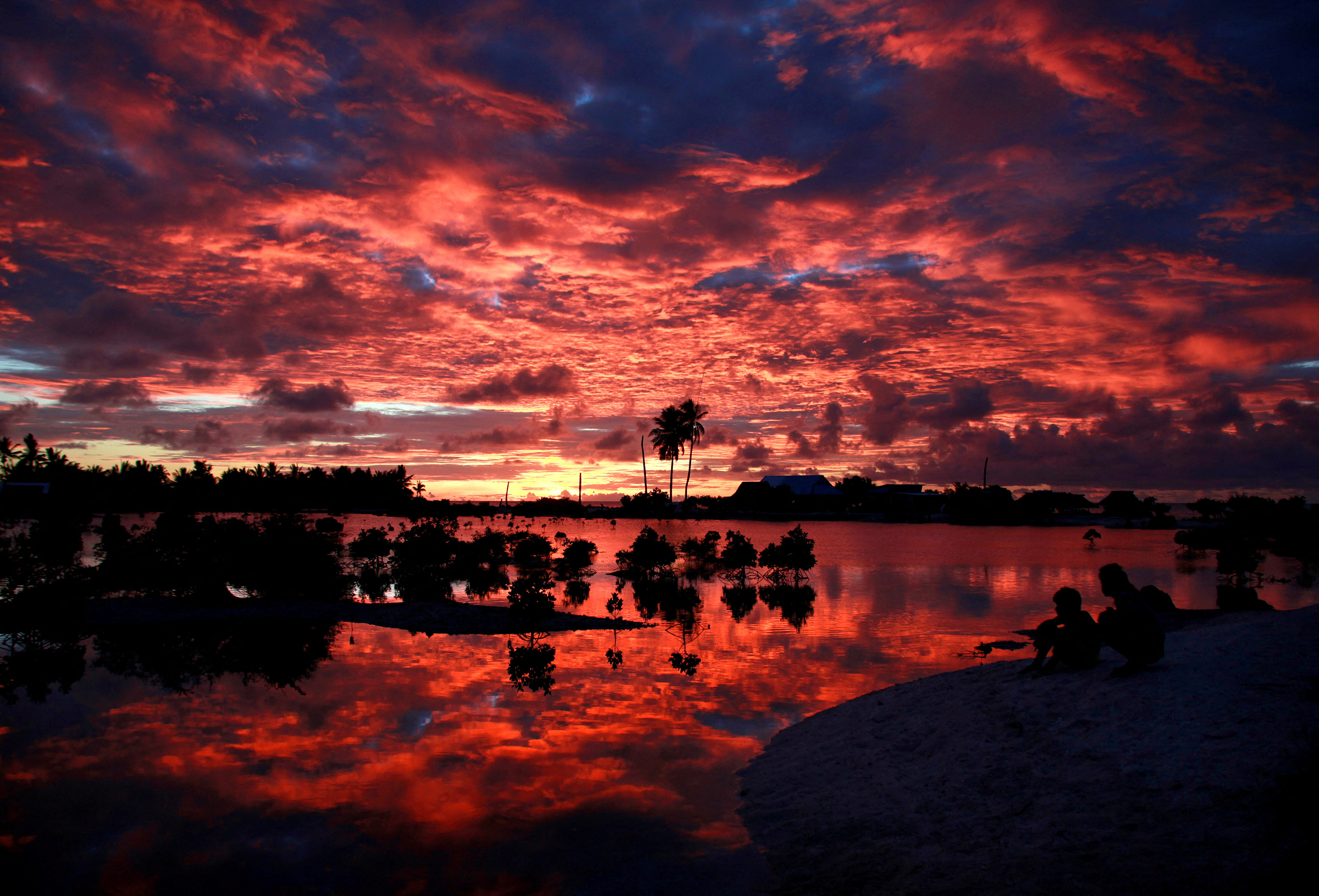 Villagers watch the sunset over a small lagoon near the village of Tangintebu on South Tarawa in the central Pacific island nation of Kiribati