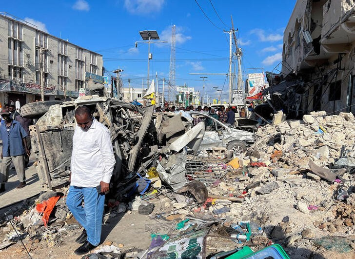 A man walks past wreckages of destroyed vehicles near the ruins of a building at the scene of an explosion along K5 street in Mogadishu