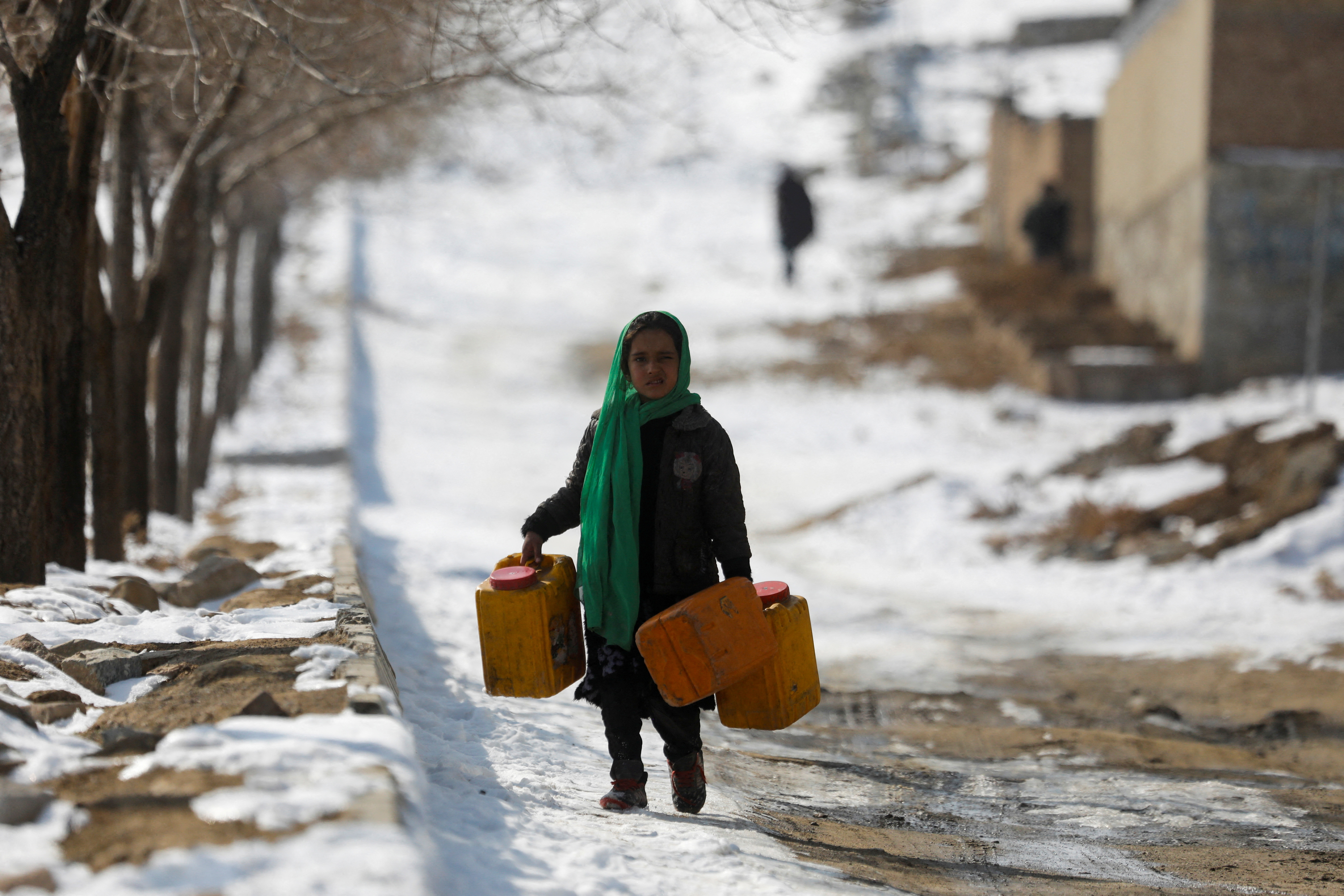 An Afghan girl carries empty water containers on a snow-covered street in Kabul