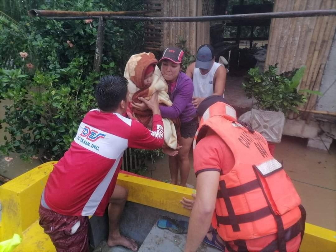 A rescuer assists a woman and her child onto a rescue boat, after the tropical storm Megi hit, in Capiz Province
