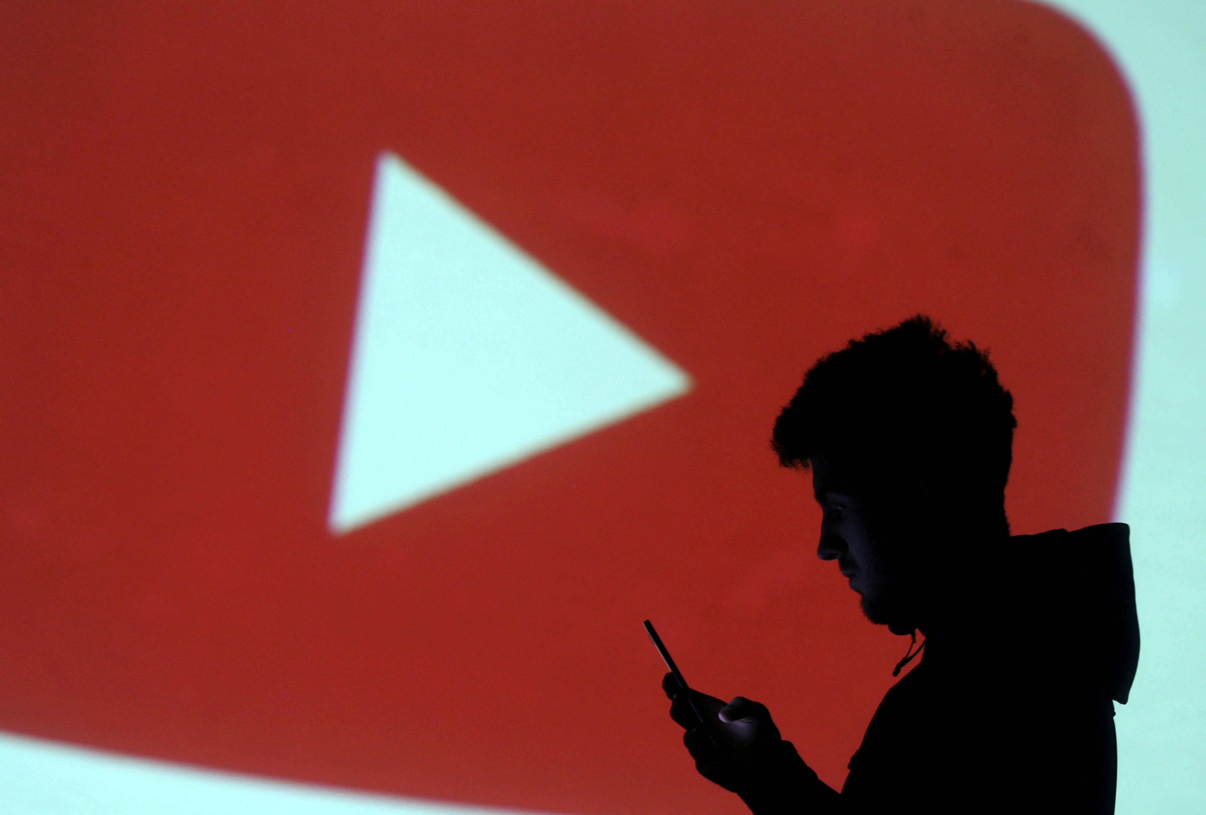 A silhouette of a mobile user is seen next to a screen projection of Youtube logo in this picture illustration