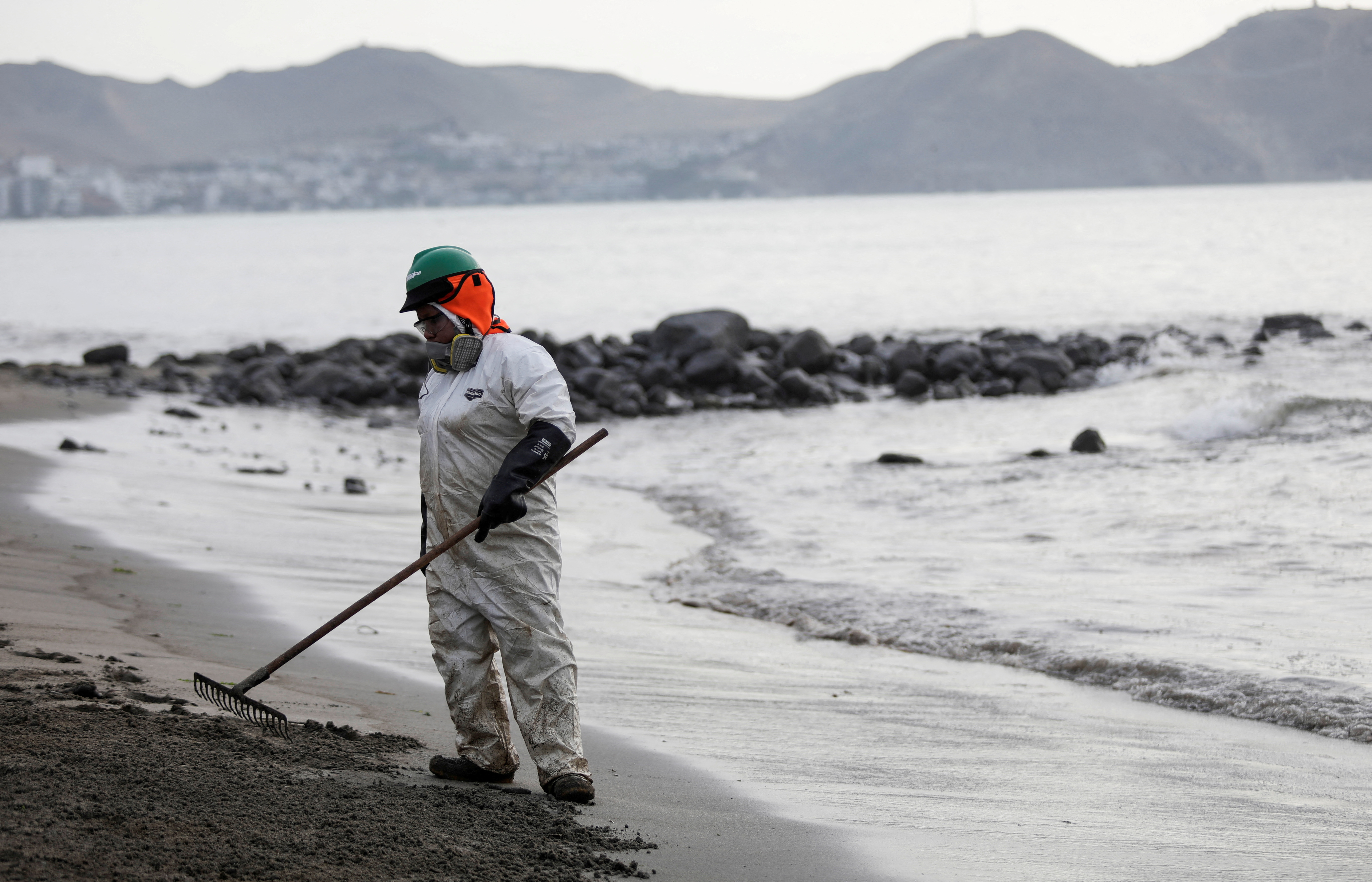 A worker cleans up an oil spill at the beach as demonstrators take part in a protest outside Repsol's La Pampilla refinery in Ventanilla