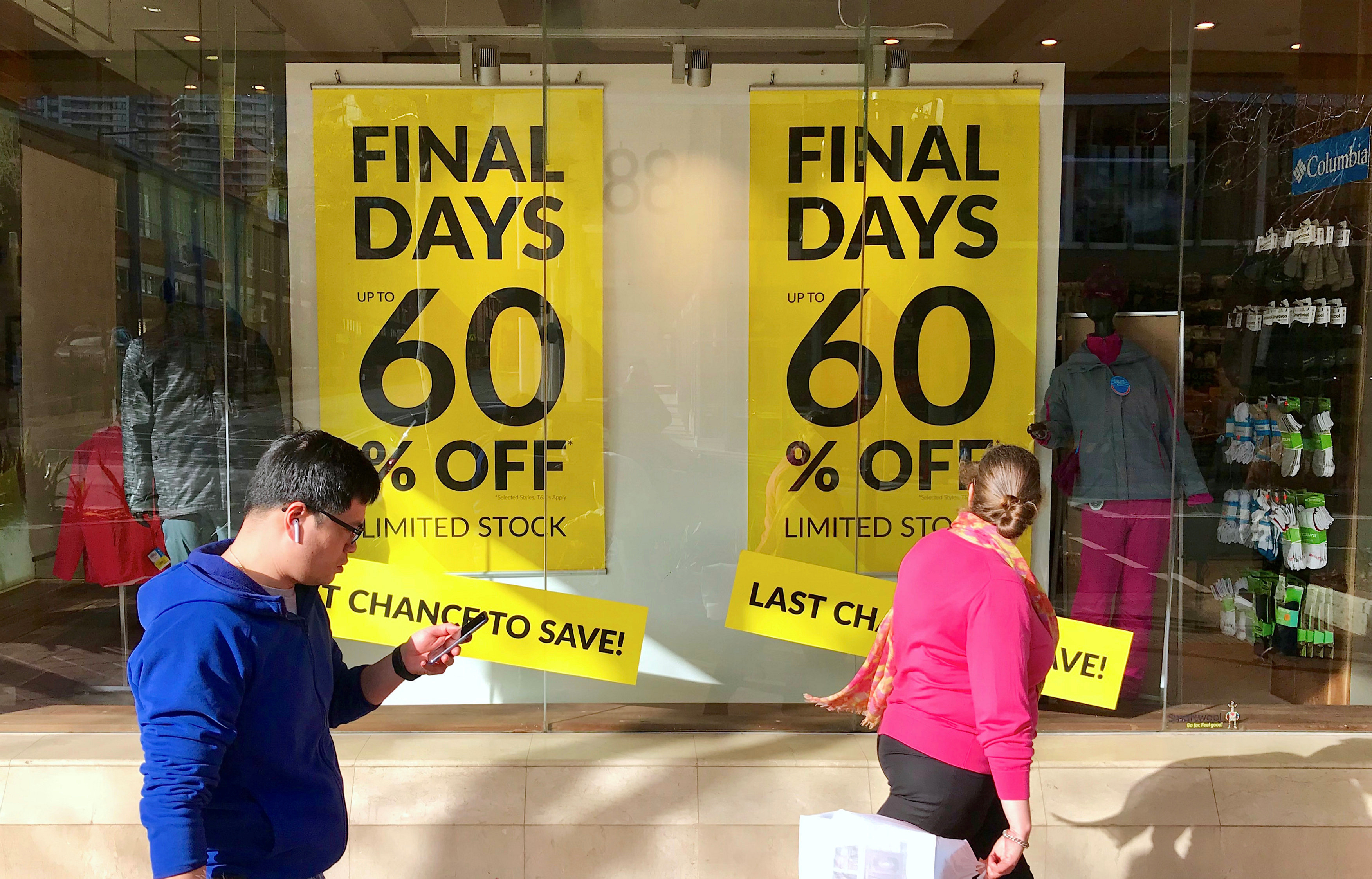 Shoppers walk past sales signs on display in the window of a retail store at a shopping mall in Sydney