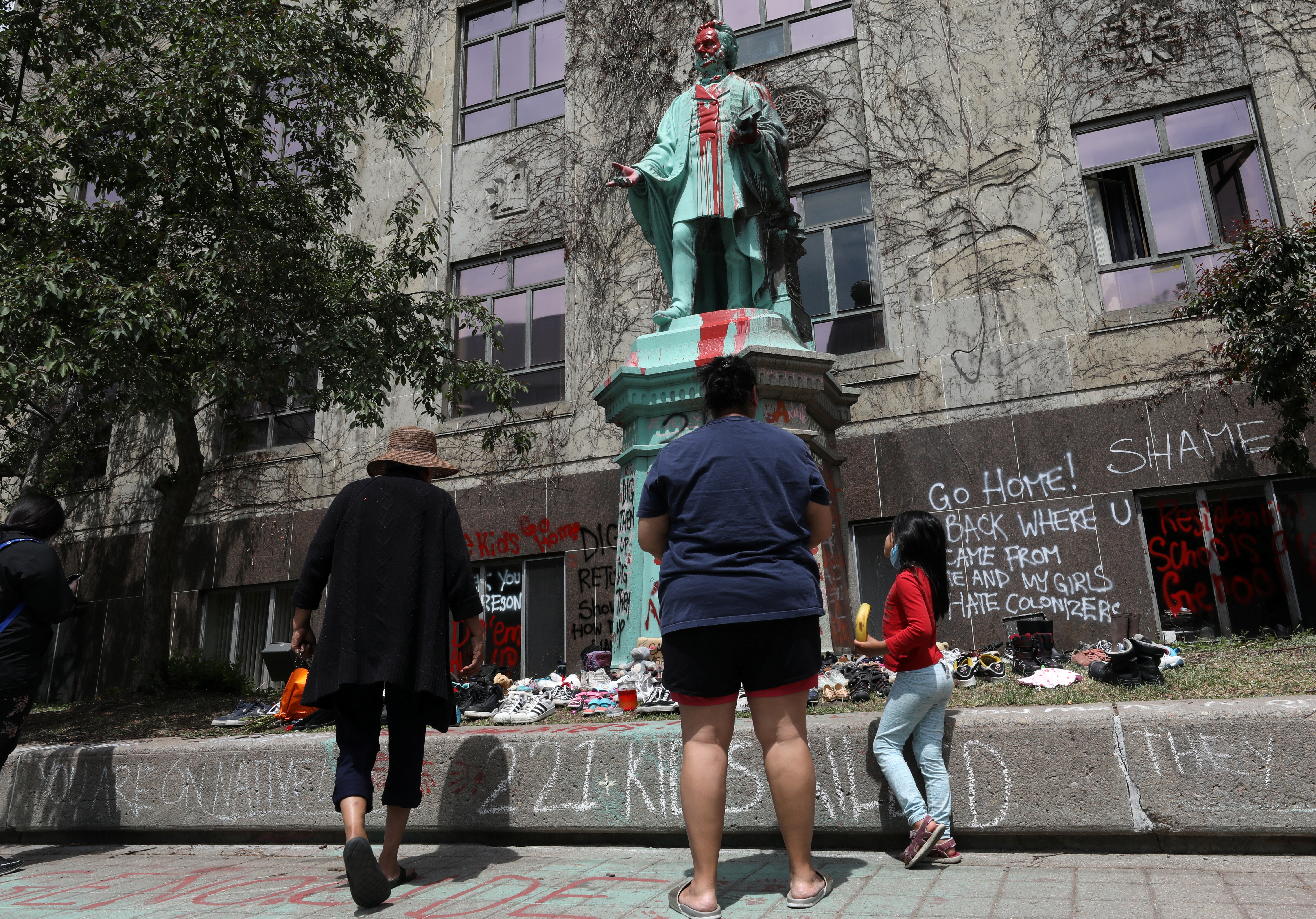 Children's shoes line the base of the defaced statue of Egerton Ryerson in Toronto
