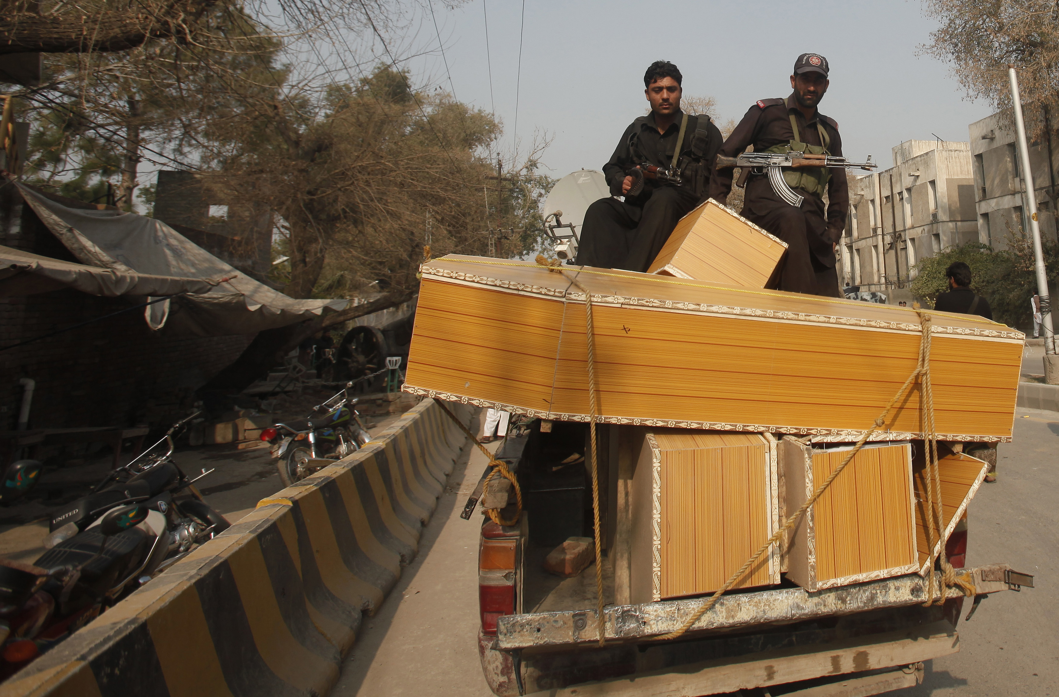 Policemen stand on a pick-up truck loaded with coffins for people who were killed after gunmen raided the compound of a senior government official in Peshawar