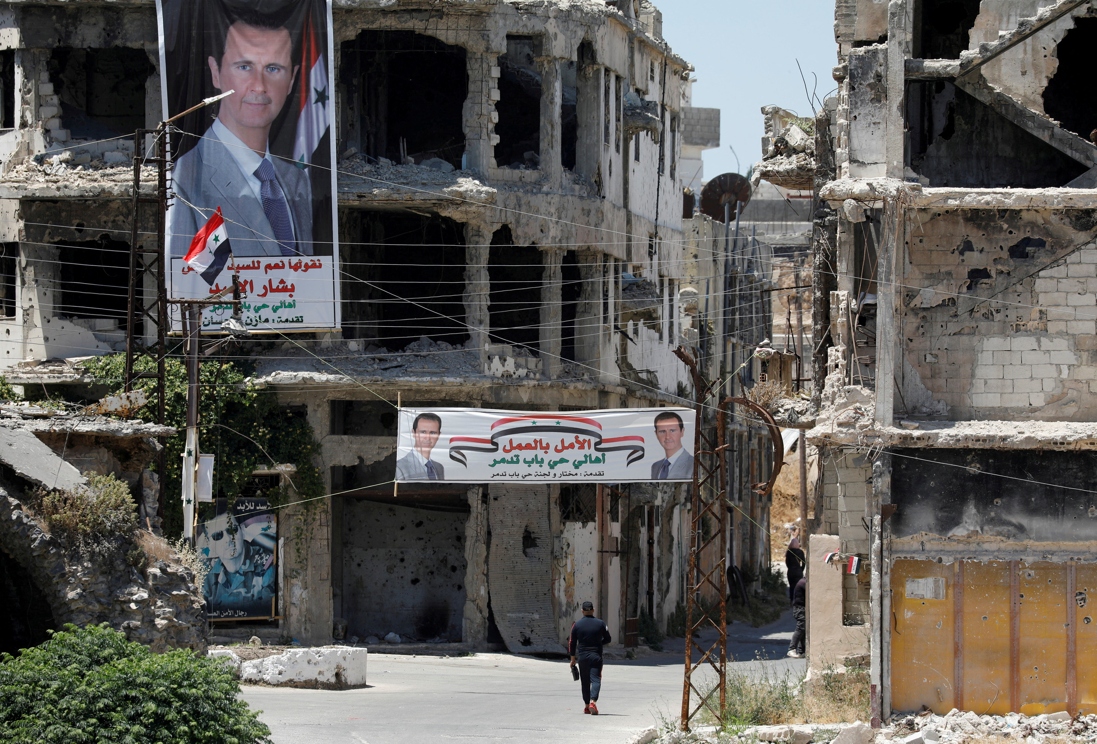 A man walks past banners depiciting Syria's President Bashar al-Assad, near damaged buildings in Homs