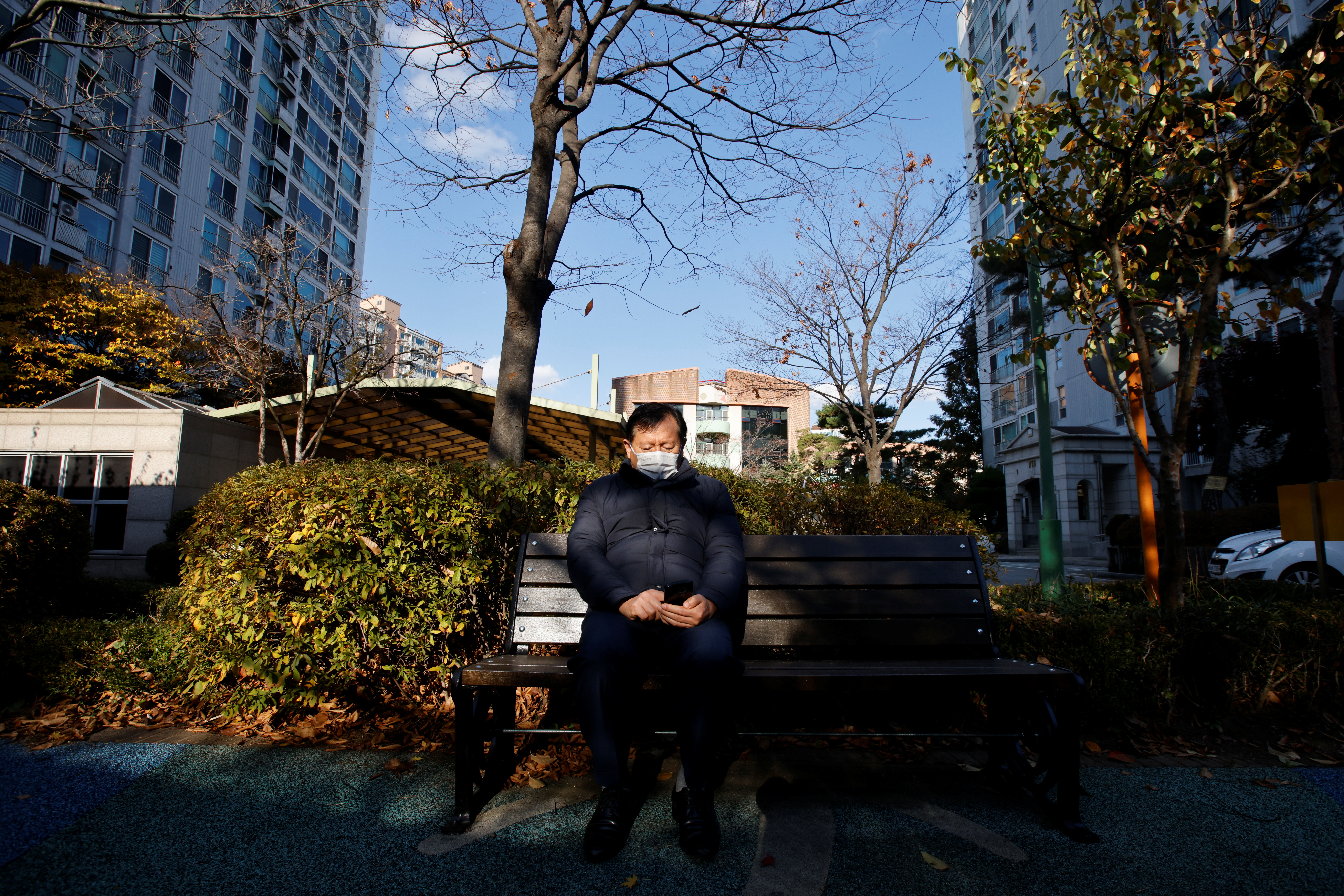Kim Gwang-ho, a former Hyundai Motor engineer, checks his cellphone in the park in front of his home in Seoul