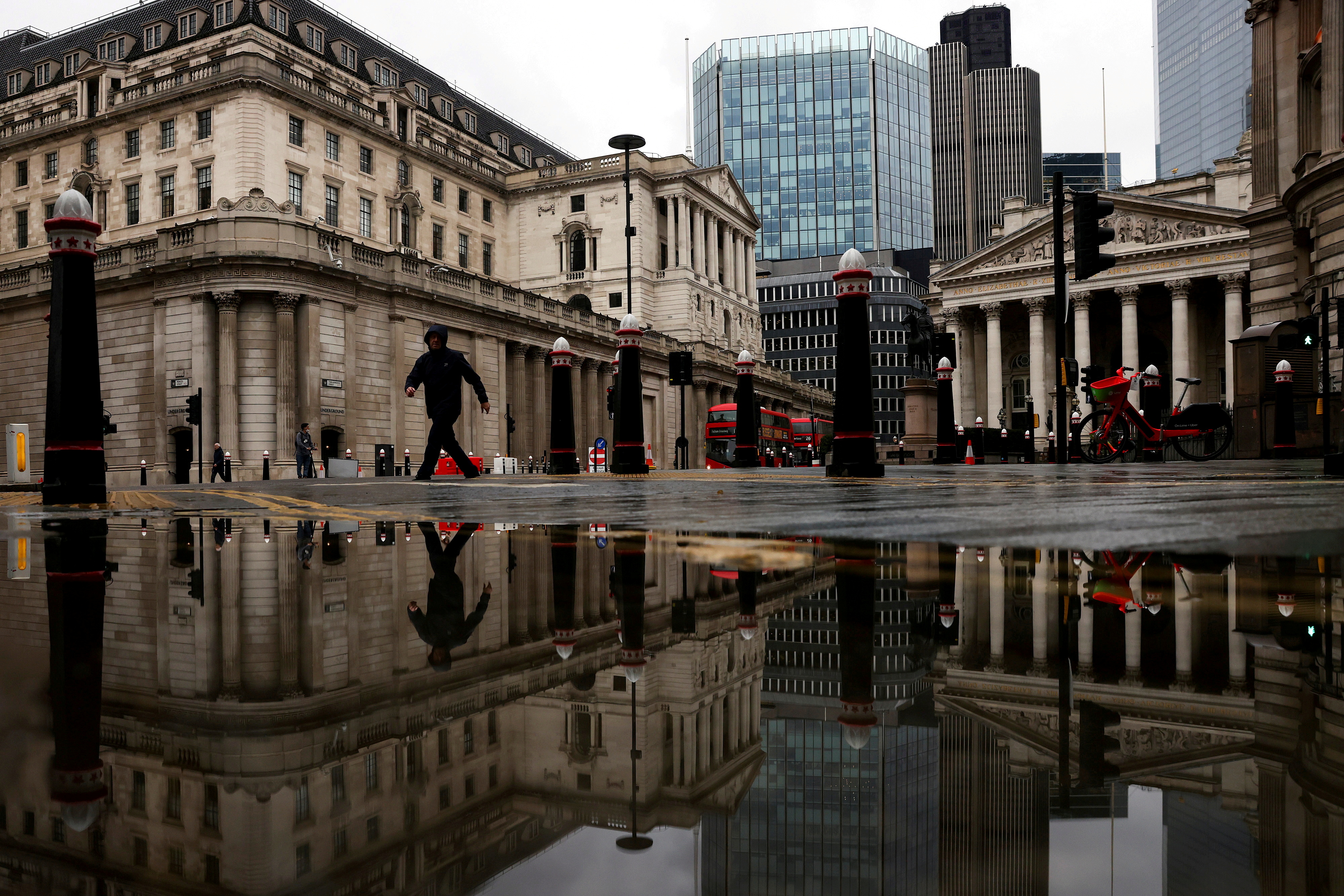 The Bank of England and Royal Exchange are reflected in a puddle as a pedestrian walks past in London