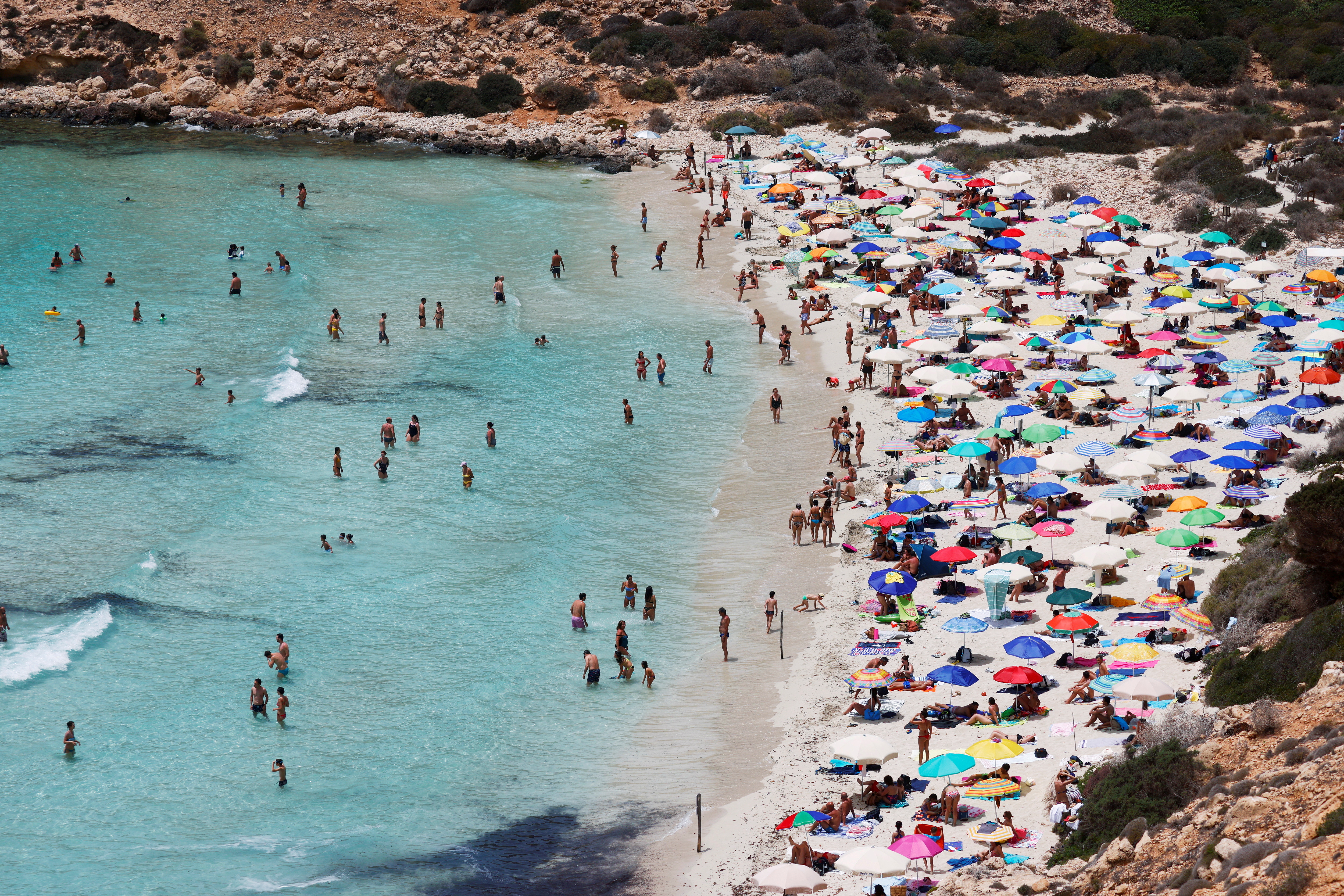 People sunbathe on the beach on the Sicilian island of Lampedusa, as a flow of migrants arriving on the Mediterranean island, in Lampedusa, Italy, June 22, 2021.