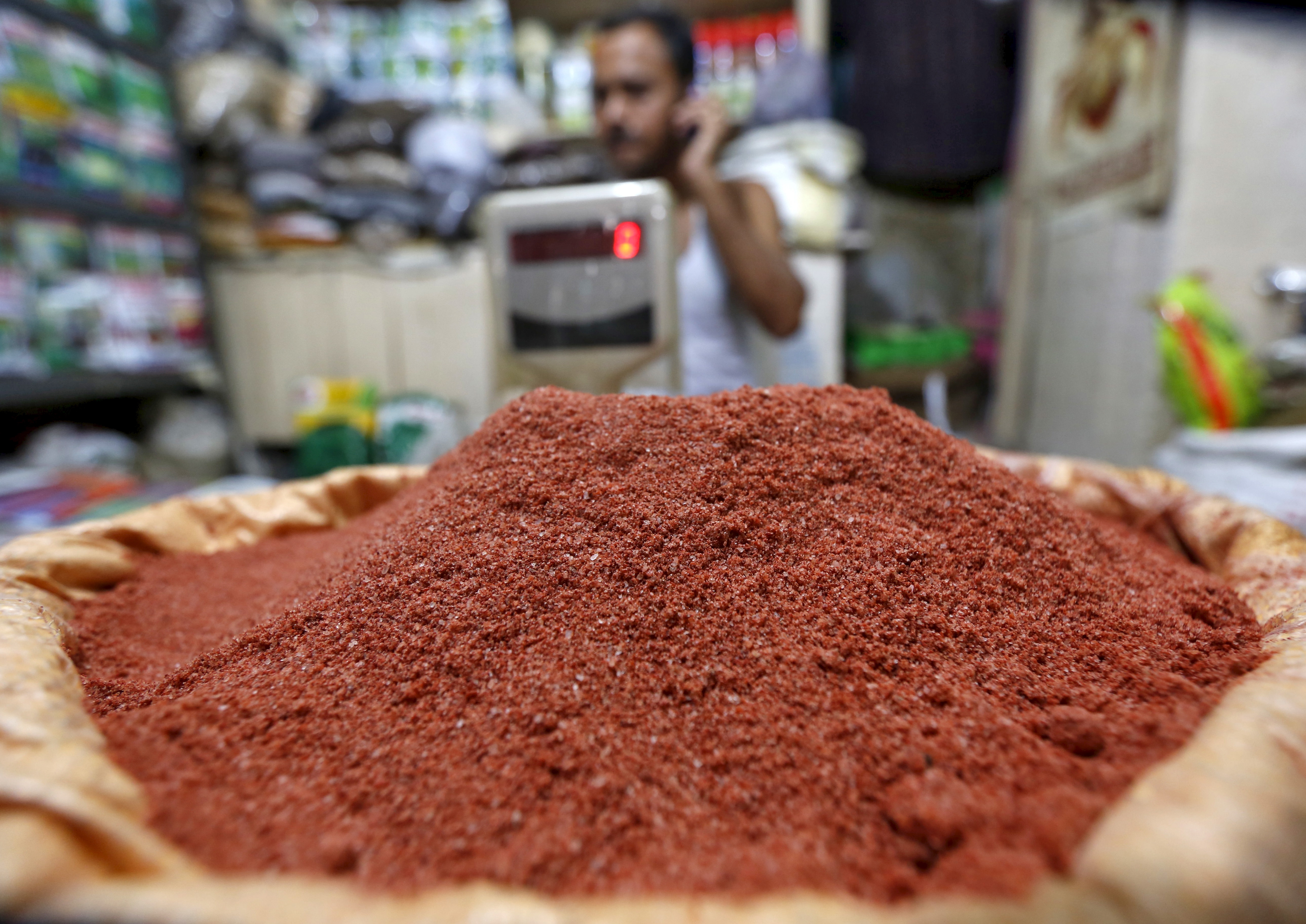 A shopkeeper speaks on his mobile phone next to a sack filled with potash for sale in Kolkata