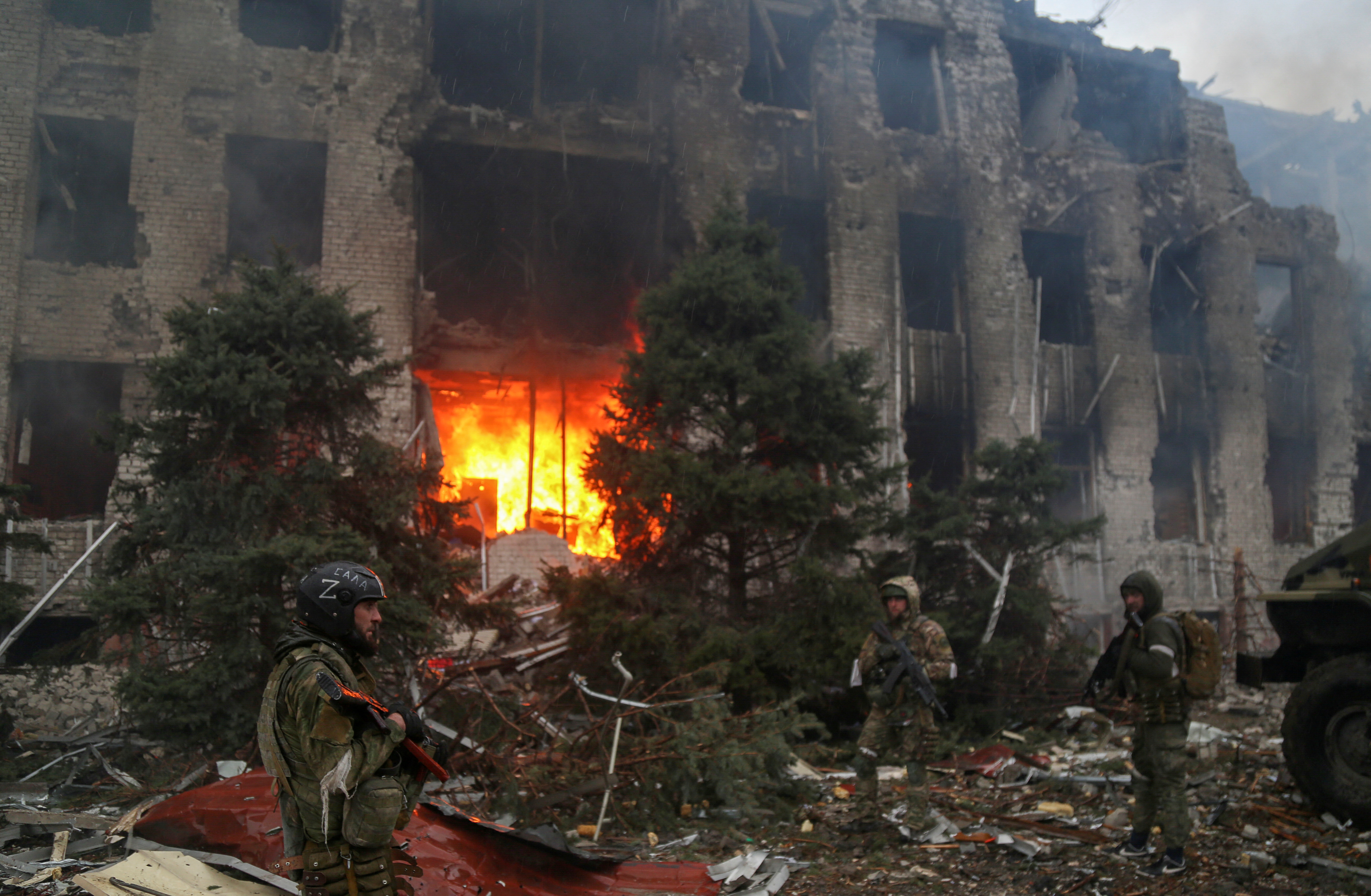 Service members of pro-Russian troops stand in front of a destroyed building in Mariupol