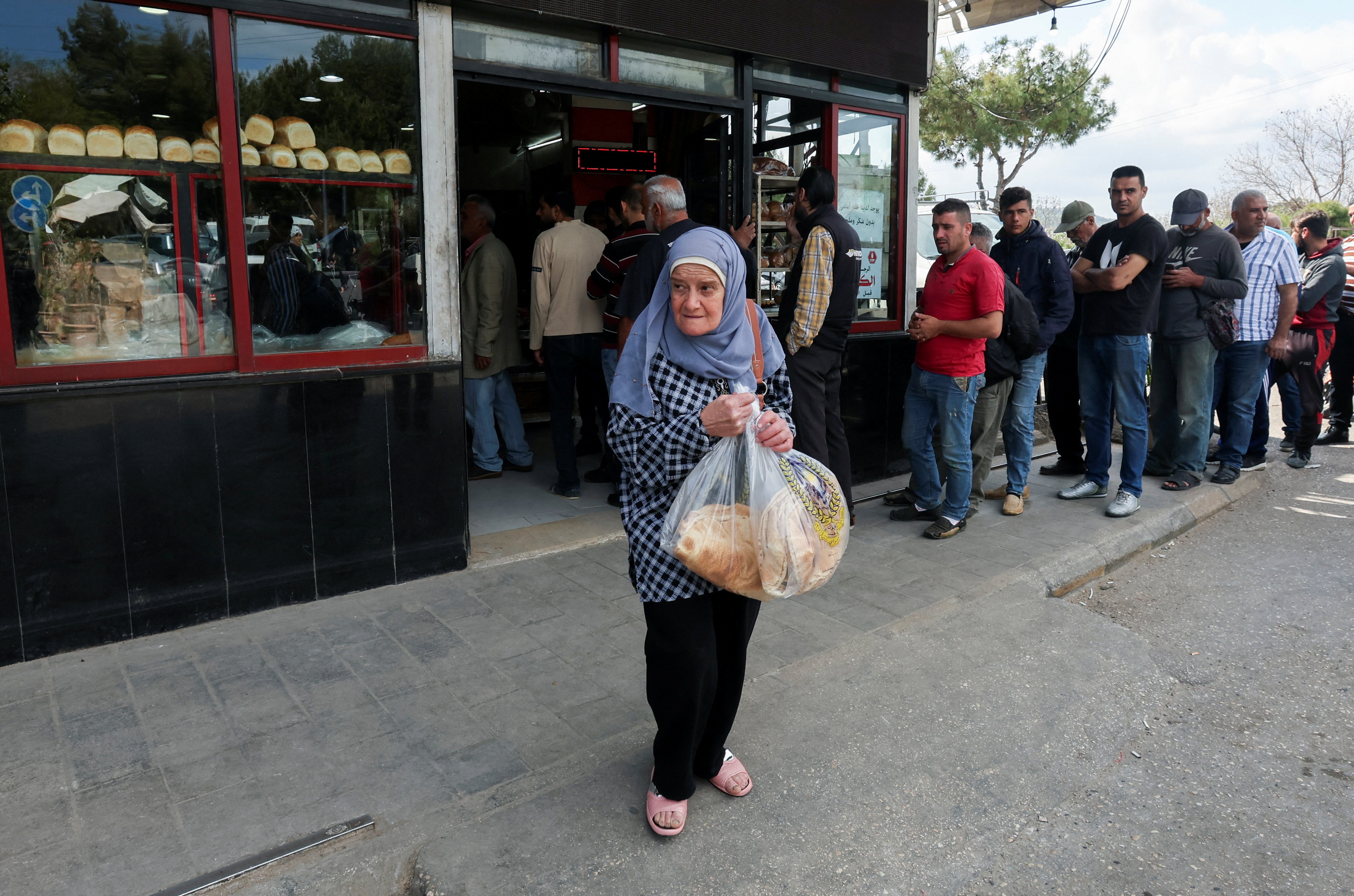 A woman carries bread as people queue outside a bakery in Sidon