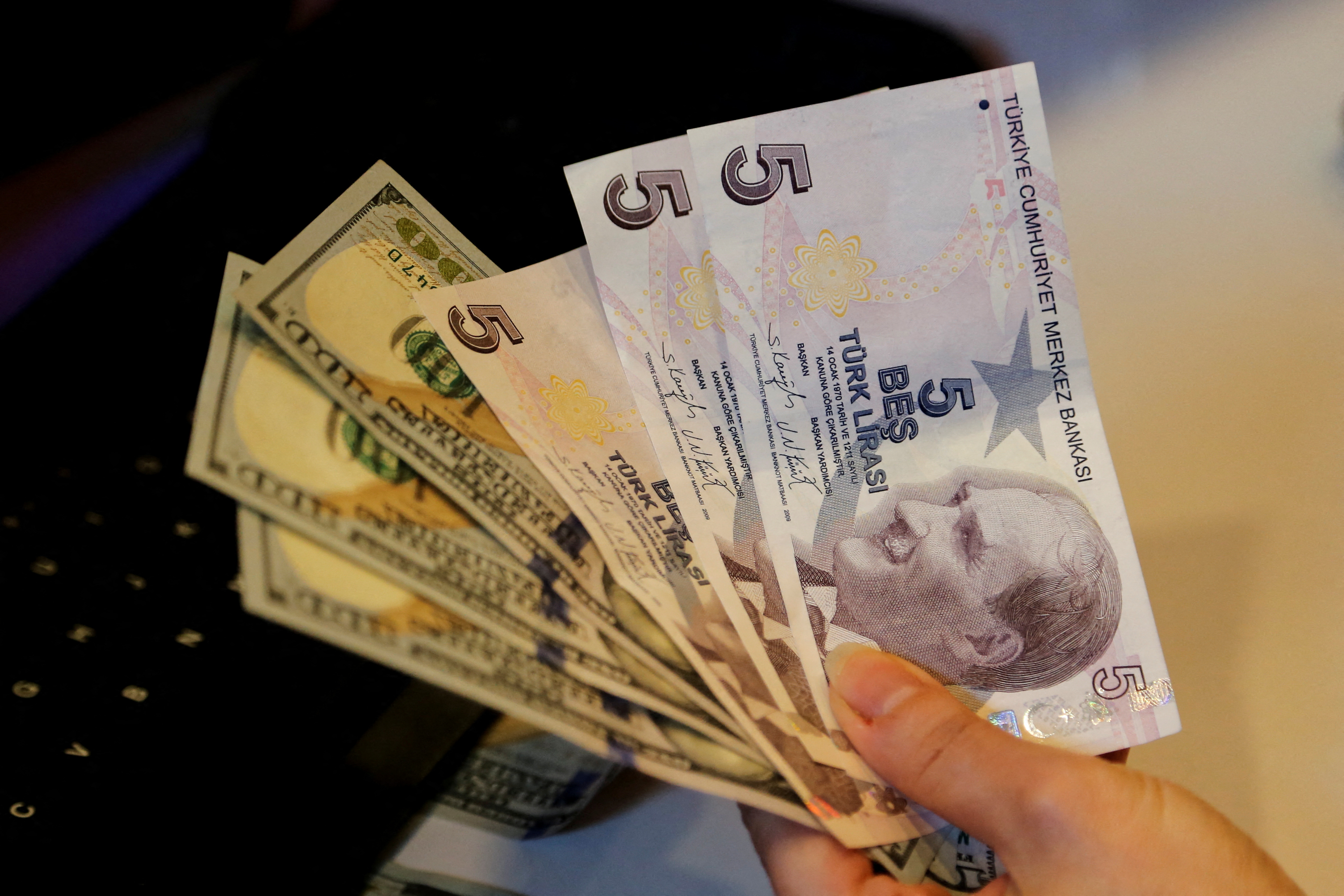 A money changer holds Turkish lira and U.S. dollar banknotes at a currency exchange office in Ankara