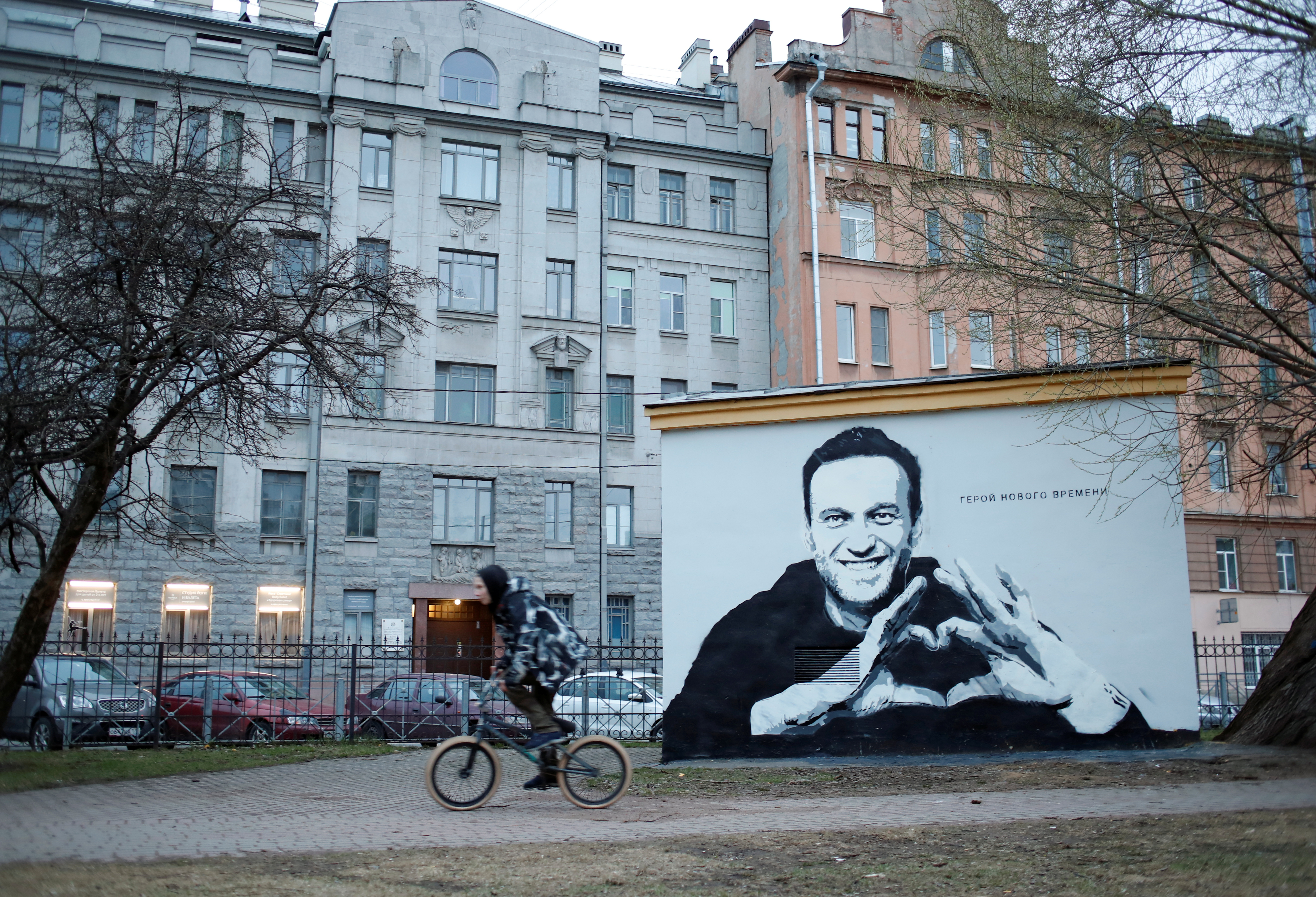 A person rides a bicycle past a graffiti depicting Alexei Navalny in Saint Petersburg