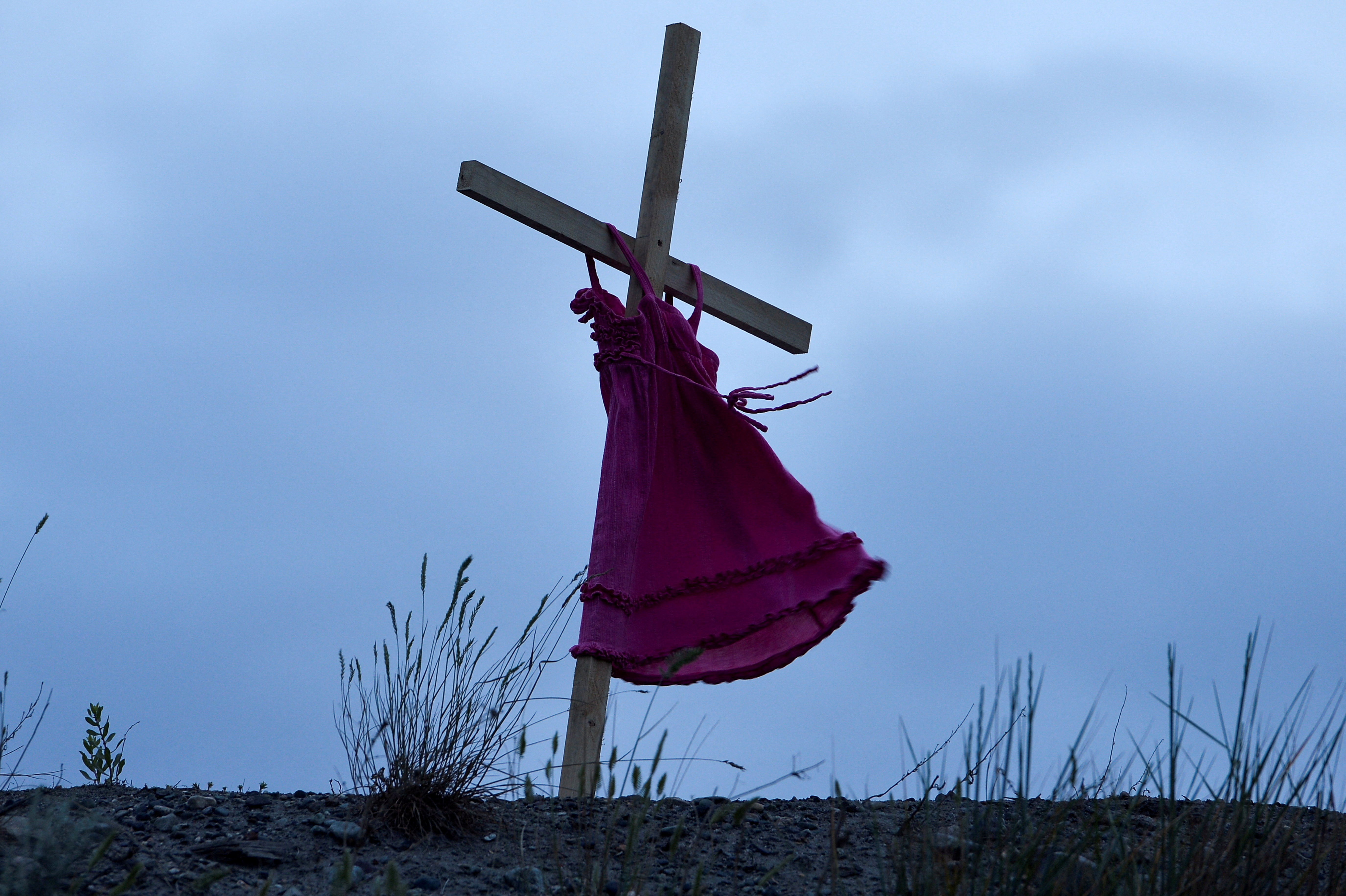 Child's red dress hangs on a stake near the former Kamloops Indian Residential School