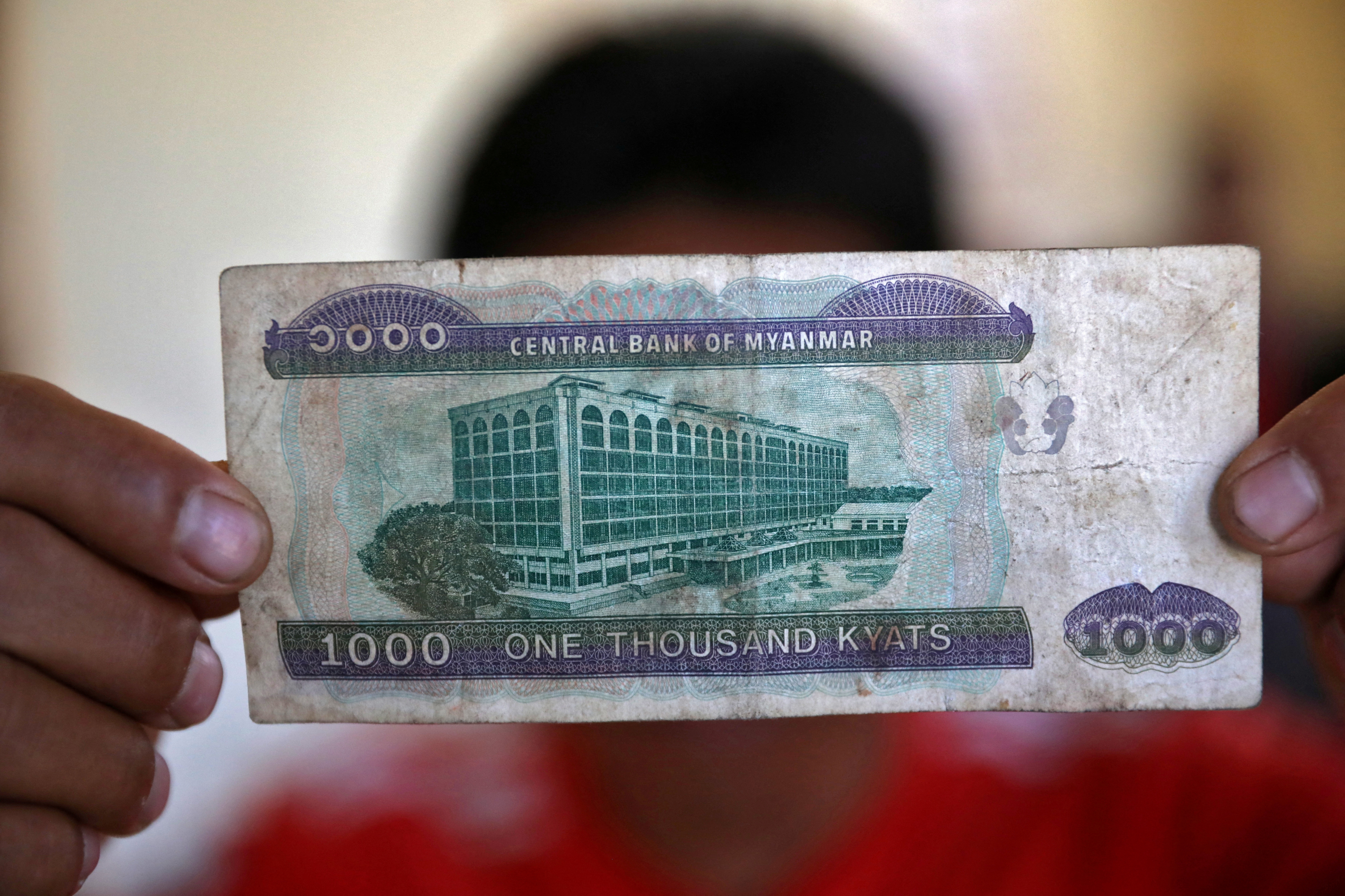 FILE PHOTO: A Myanmar national who said he was a fireman and recently fled to India shows a Myanmar kyat banknote as he poses at an undisclosed location
