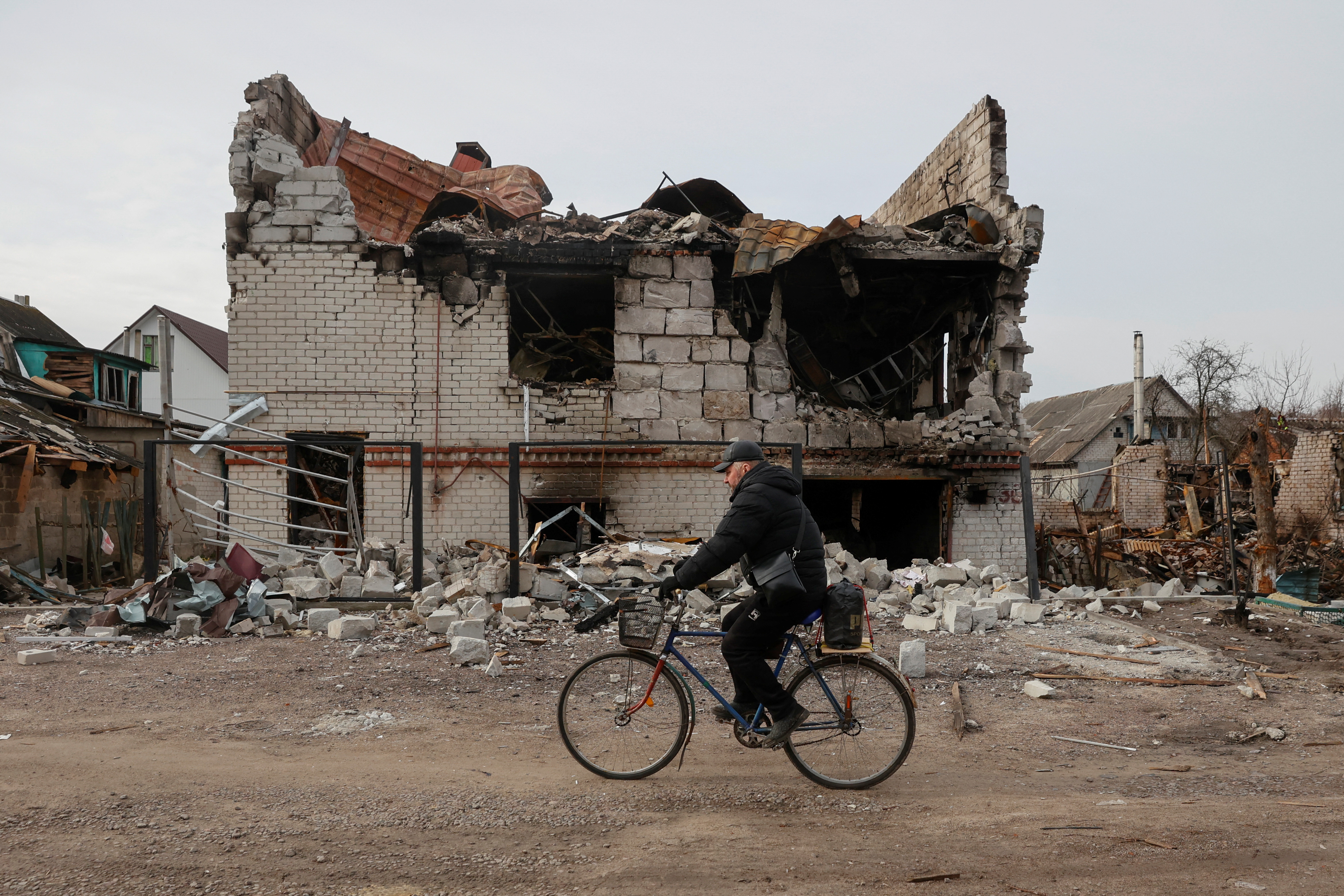 A local man rides a bicycle past a house damaged by heavy shelling and airstrikes in Chernihiv