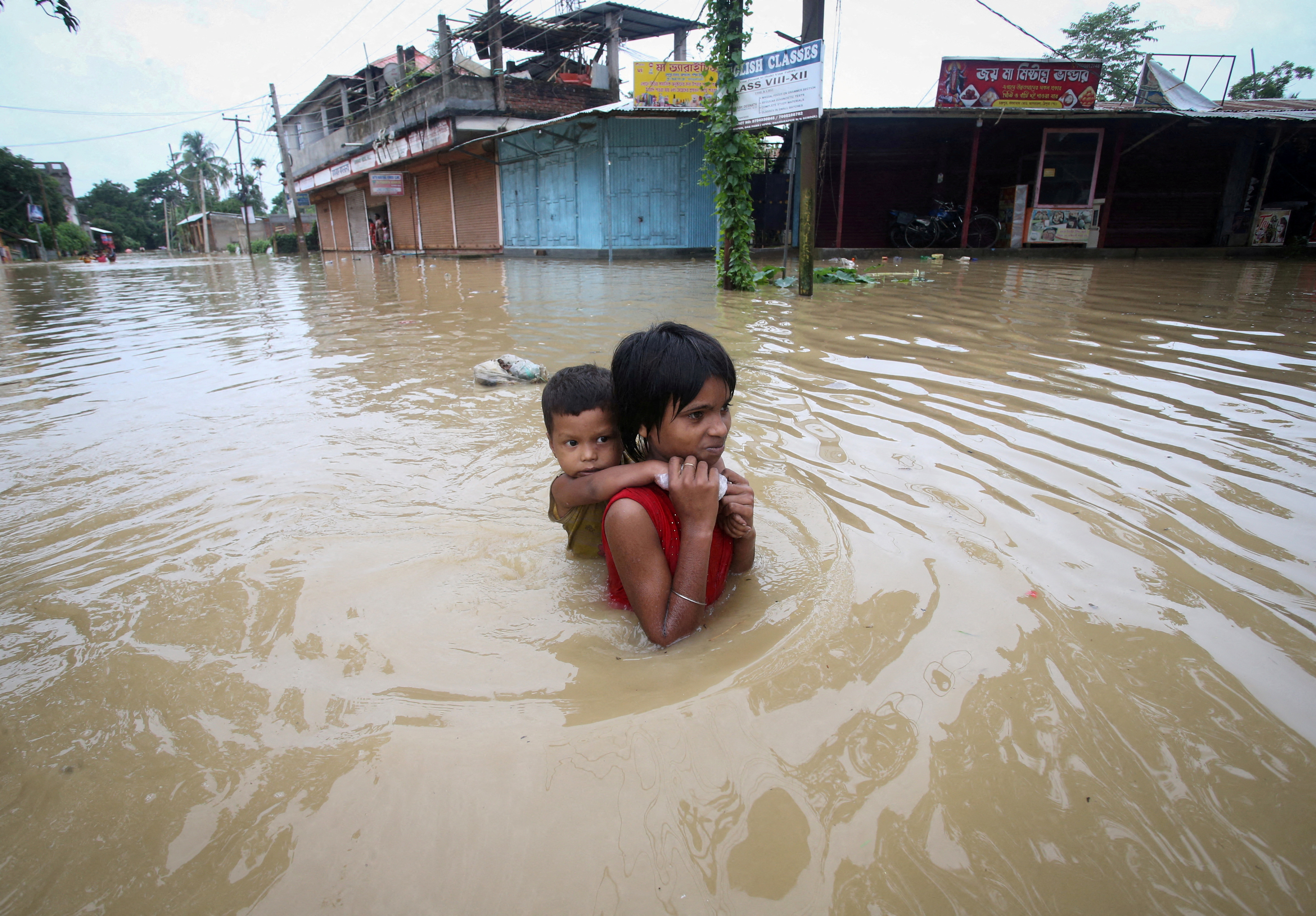 A girl carries her brother as she wades through a flooded road after heavy rains on the outskirts of Agartala