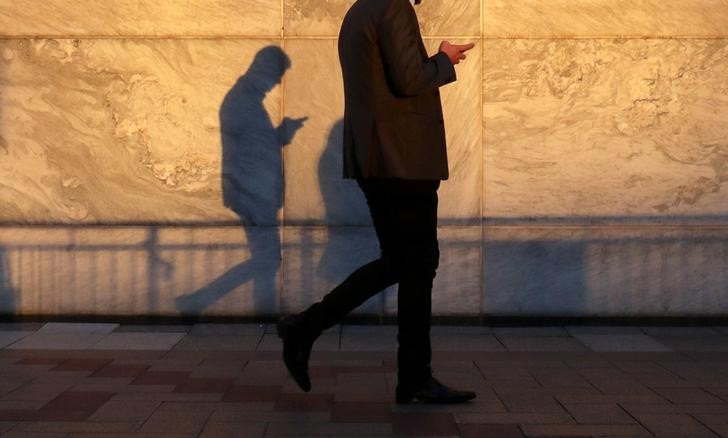 An unidentified man using a smart phone walks through London's Canary Wharf financial district in the evening light in London