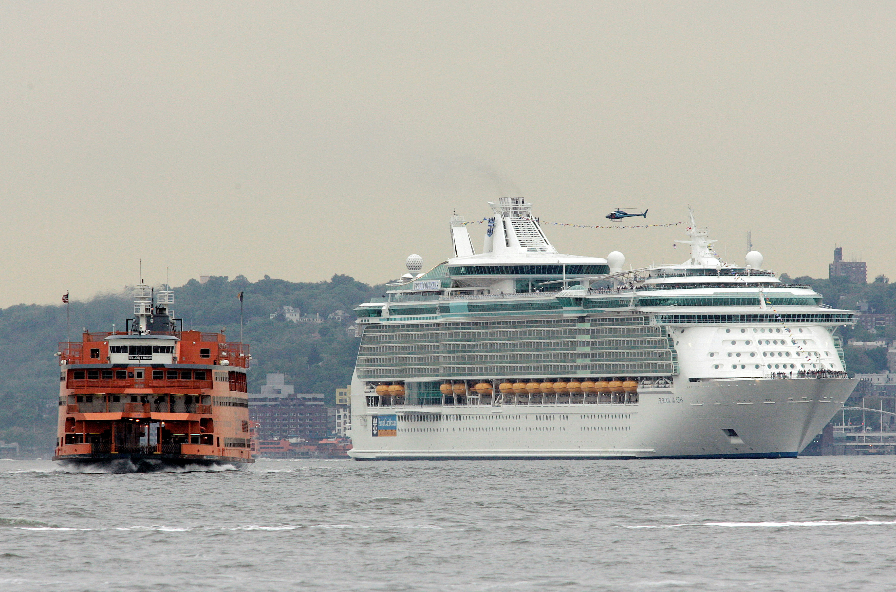 Staten Island Ferry cruises past Royal Caribbean cruise ship Freedom of the Seas as it makes its way up Hudson River in New York