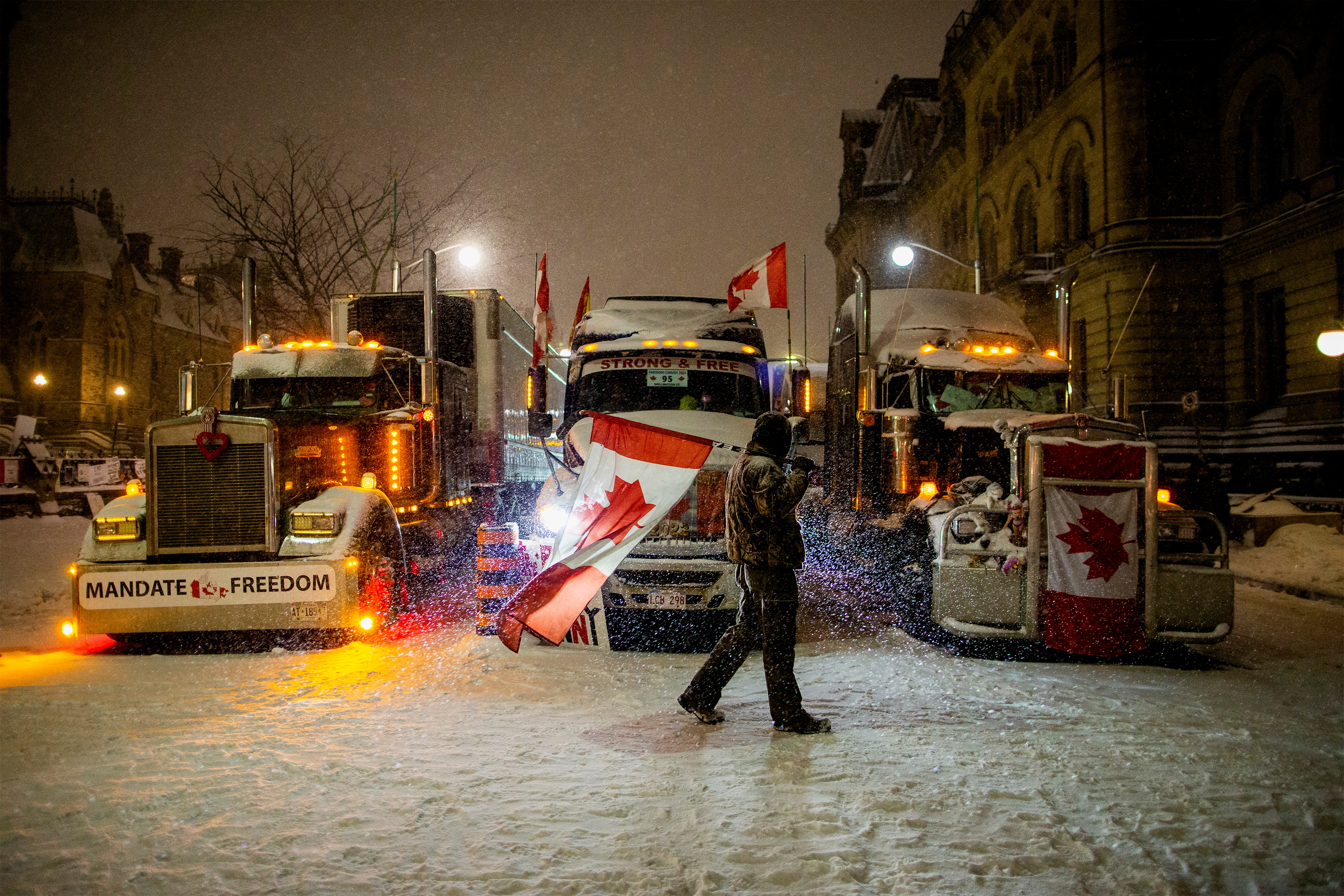 Un uomo cammina con una bandiera del Canada davanti a un camion mentre le proteste contro i mandati del vaccino contro la malattia del coronavirus (COVID-19) continuano, lungo Wellington Street, vicino al Parlamento del Canada, a Ottawa, Ontario, Canada, 17 febbraio 2022. REUTERS/Carlos Osorio