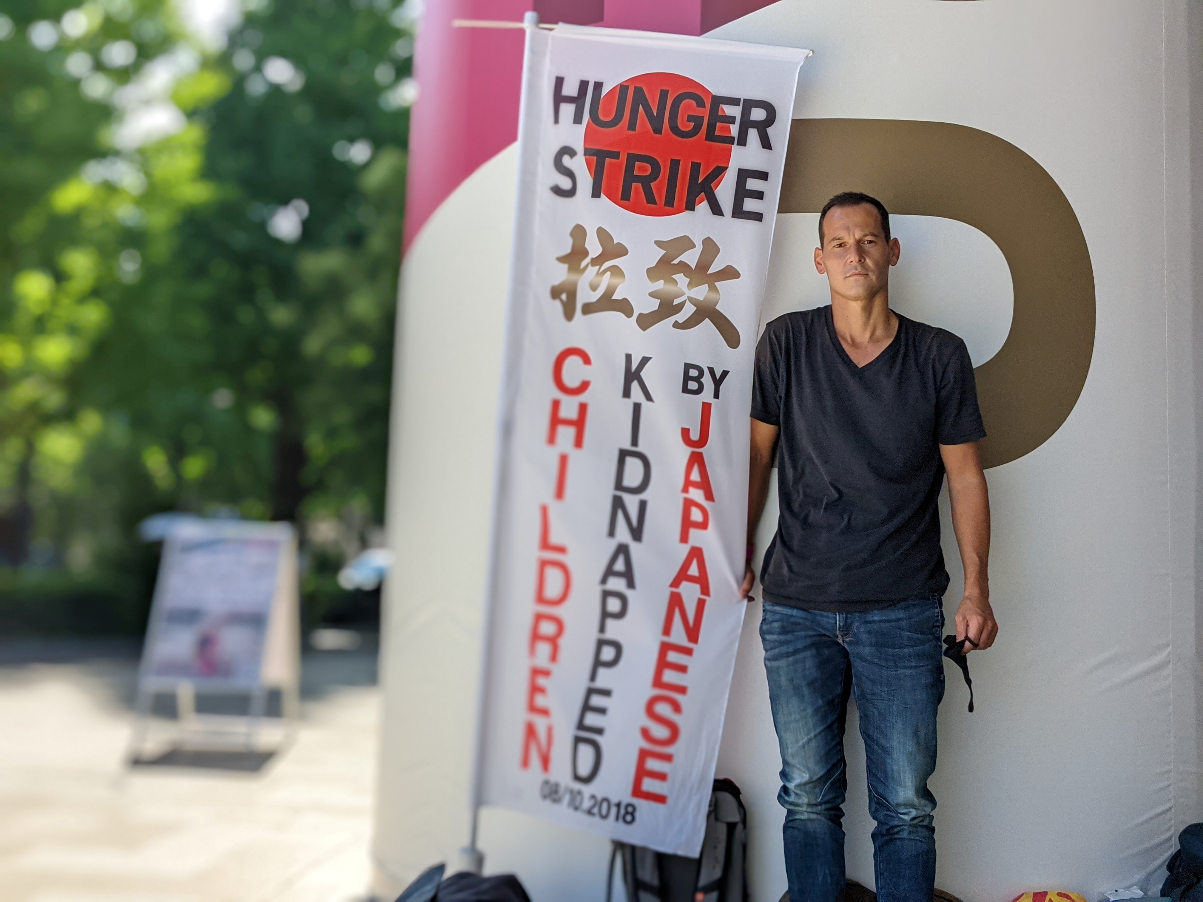 French father-of-two Vincent Fichot stands with his banner where he has been on a hunger strike since July 10 to protest what he says is Japan's sanctioning of child 'abductions' by a parent, near the Olympic Stadium in Tokyo, Japan July 21, 2021.  REUTERS/Chang-Ran Kim