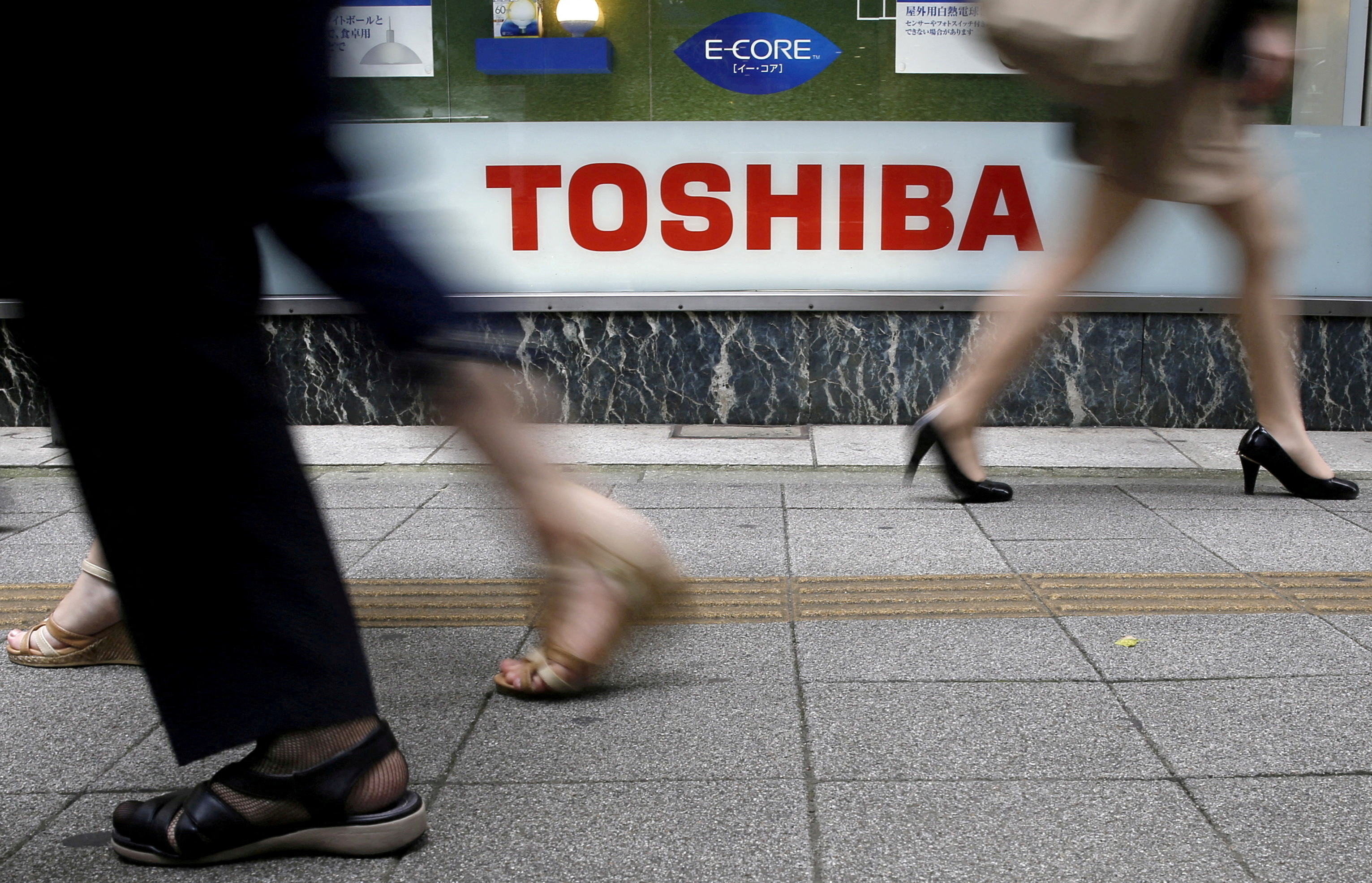Pedestrians walk past a Toshiba logo outside an electronics retailer in Tokyo