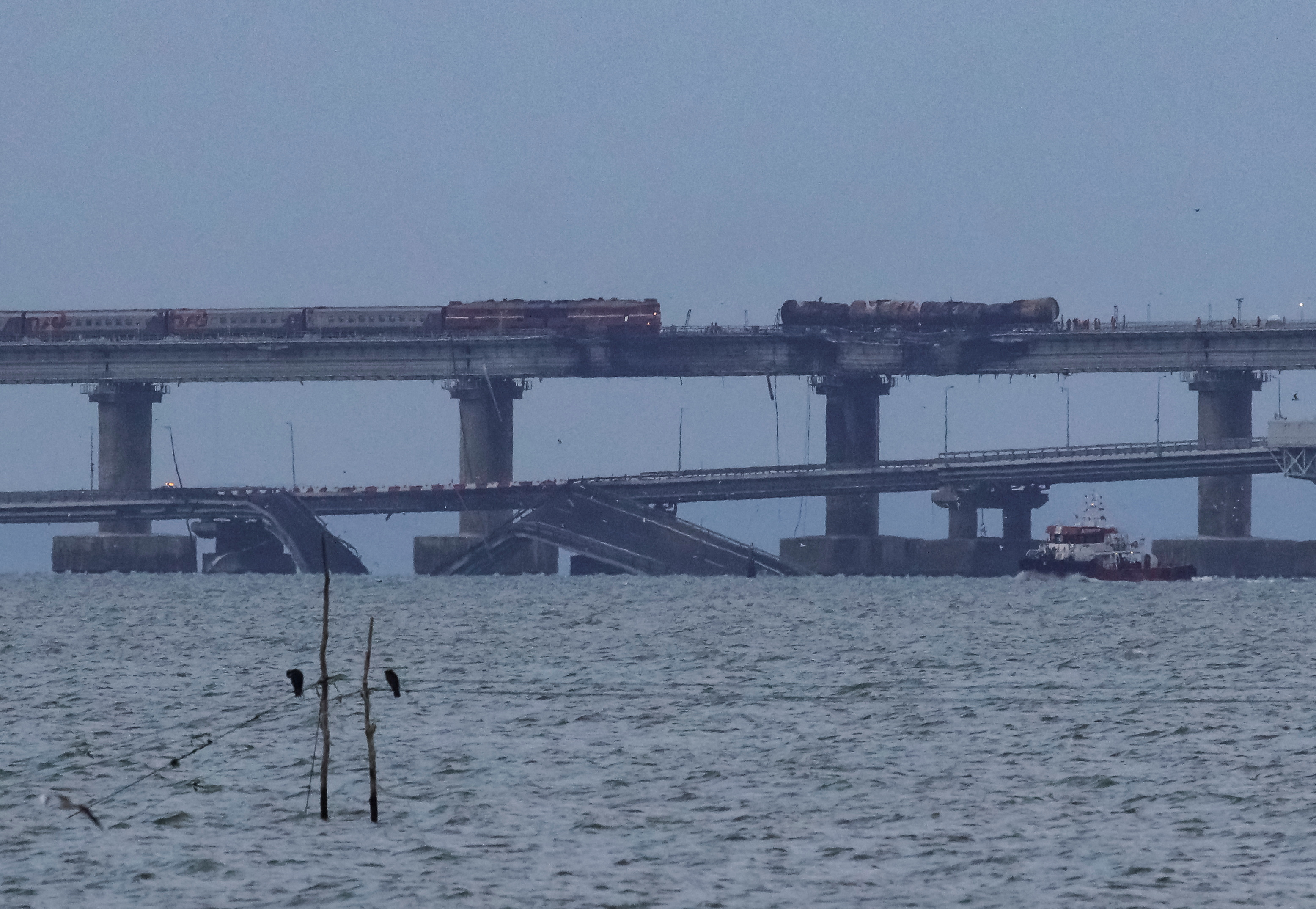 A passenger train approaches fuel tanks burnt on the Kerch bridge, after an explosion destroyed part of it, in the Kerch Strait, Crimea