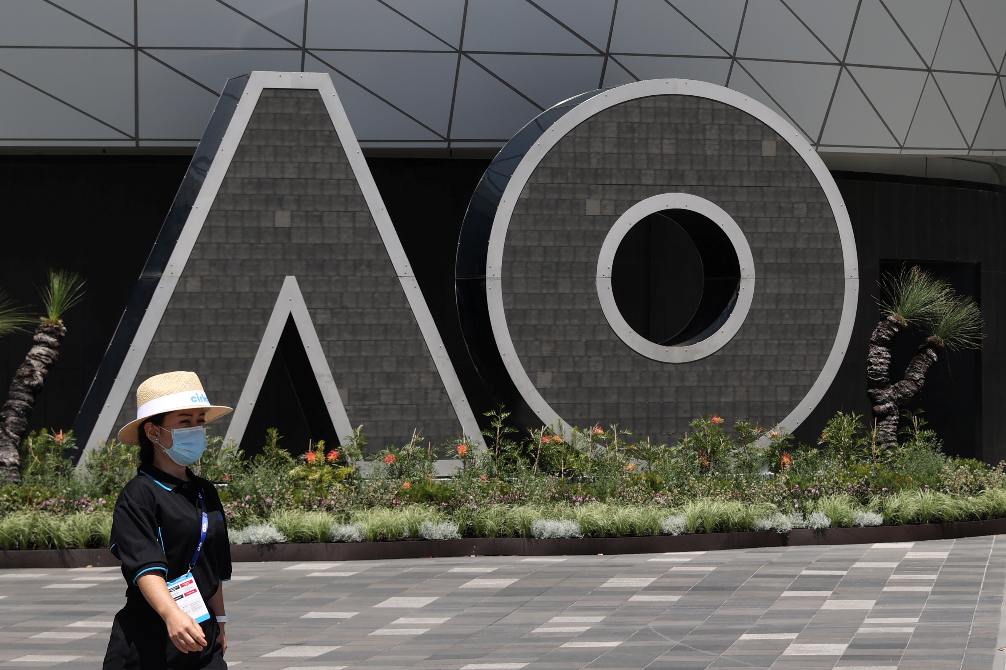 A person wearing a protective face mask walks past an Australian Open logo at Melbourne Park in Melbourne