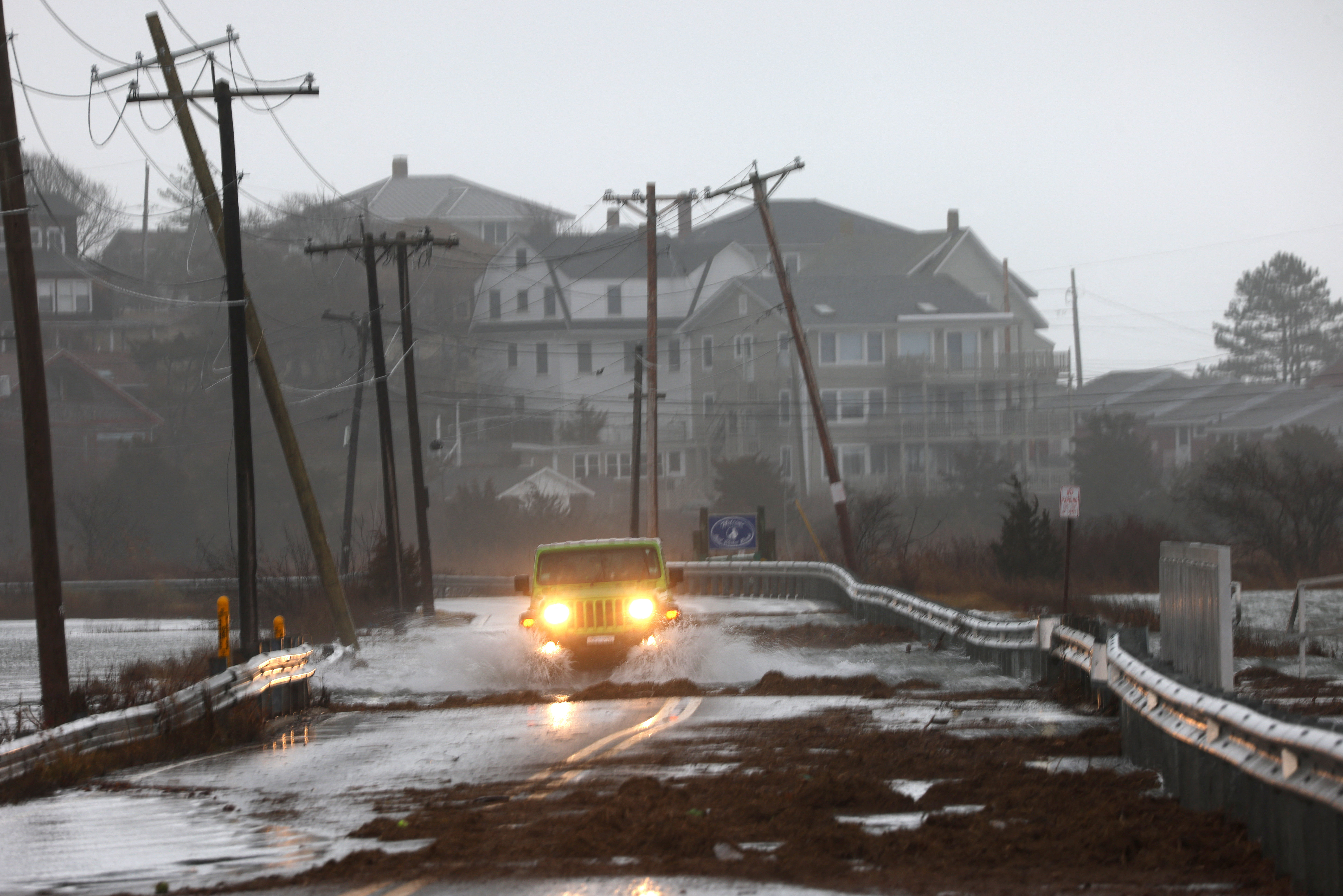 A driver drives through a flooded road at high tide during a winter storm in Gloucester