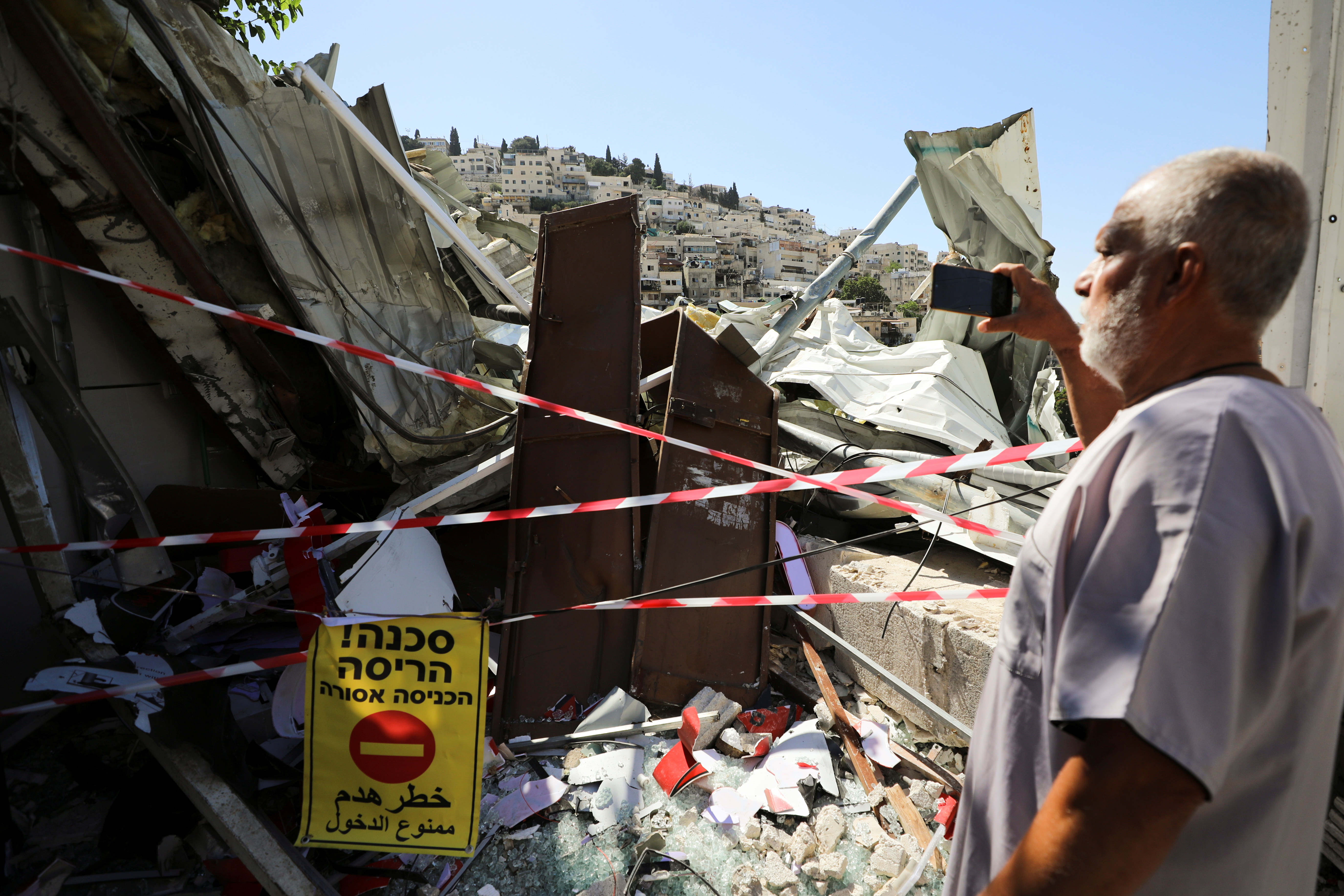 A Palestinian man uses his mobile phone as he stands near the debris of a shop that Israel demolished in the Palestinian neighbourhood of Silwan in East Jerusalem