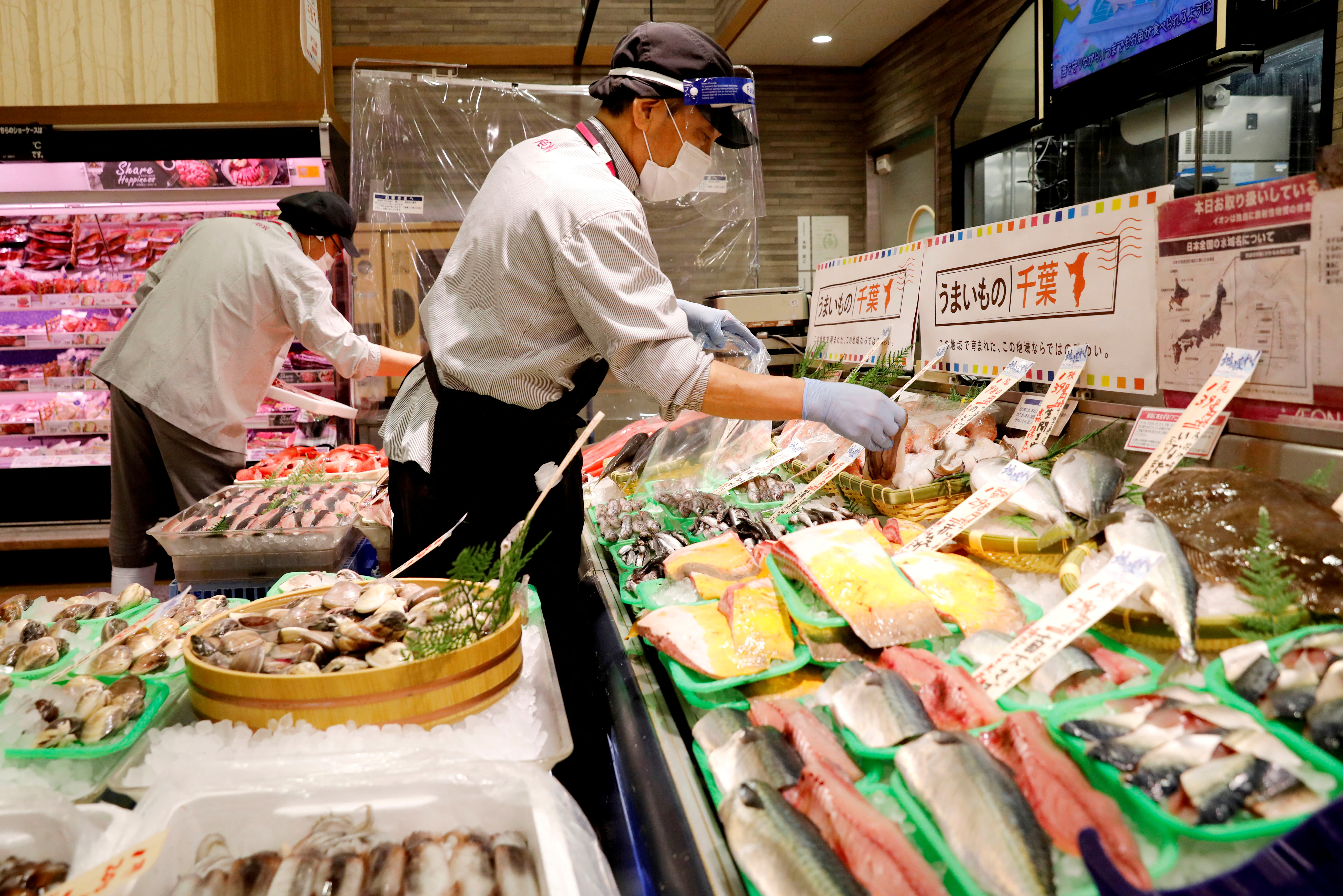 A worker wearing a face shield sells fish at a Japanese supermarket