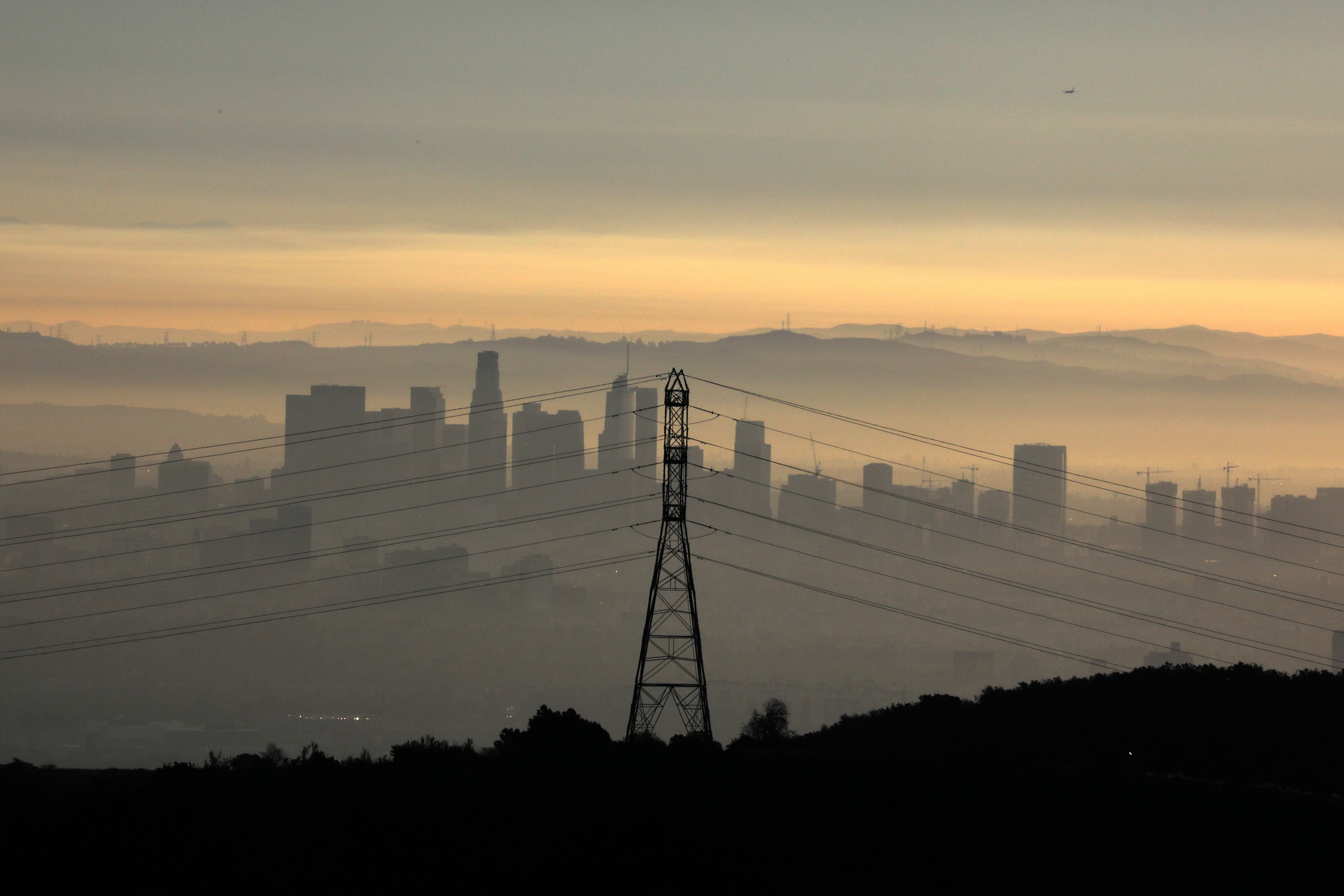 The downtown Los Angeles skyline is seen behind an electricity pylon at sunrise in Los Angeles