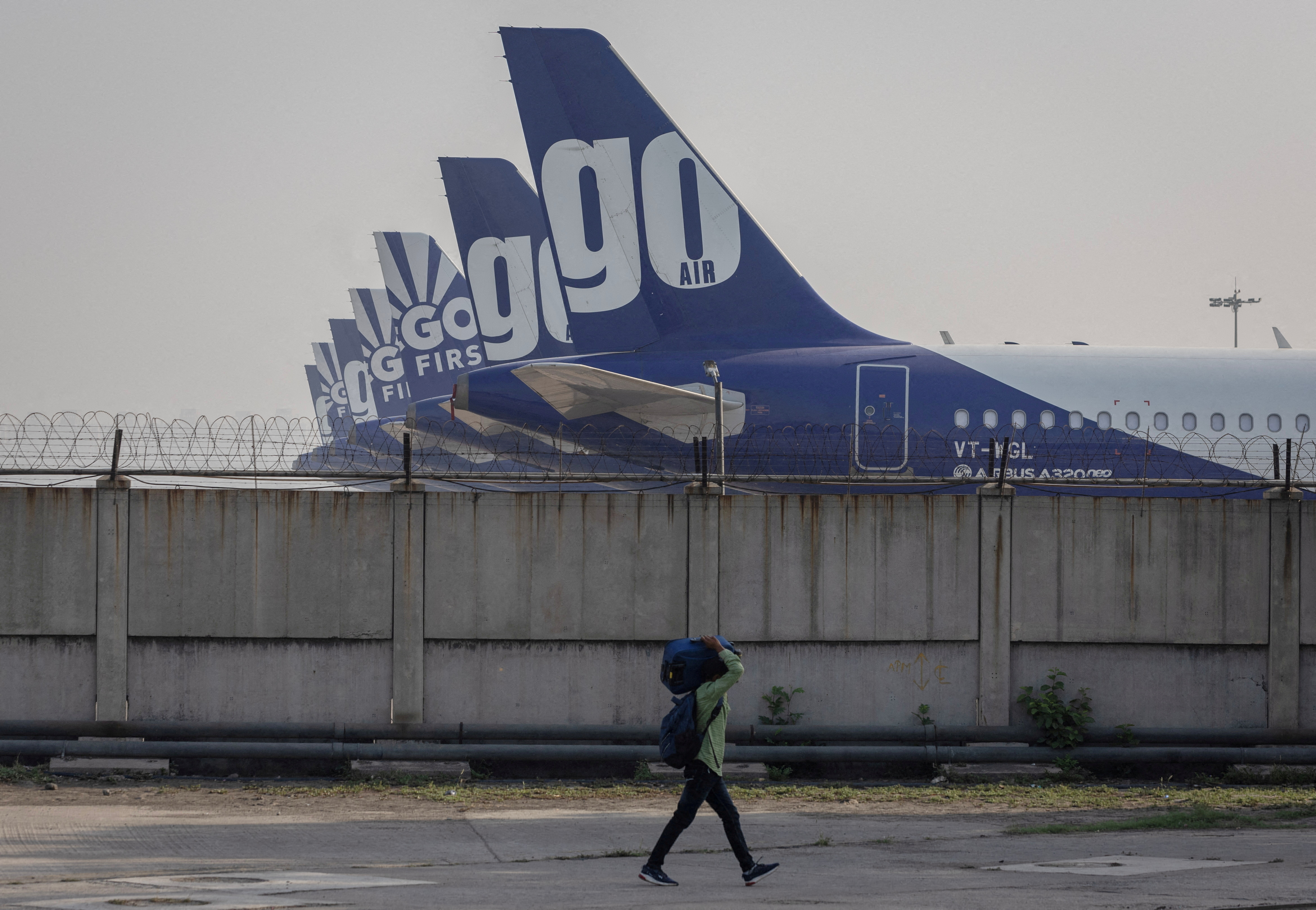A man carries his bag as he walks past the Go First airline, formerly known as GoAir, passenger aircrafts parked on the tarmac at the airport in New Delhi