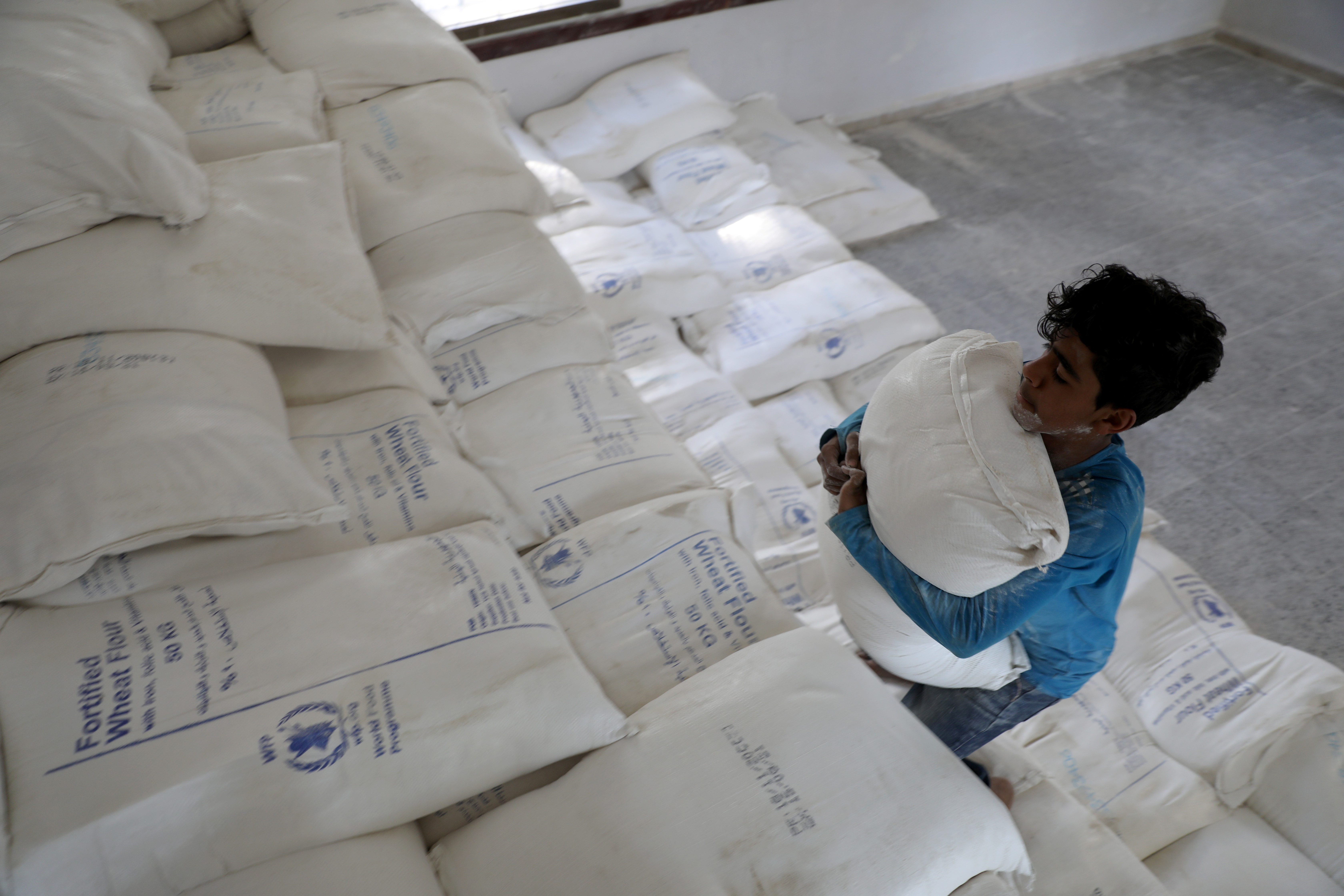 Worker carries a sack of wheat flour at a foodstuff aid distribution center in Sanaa