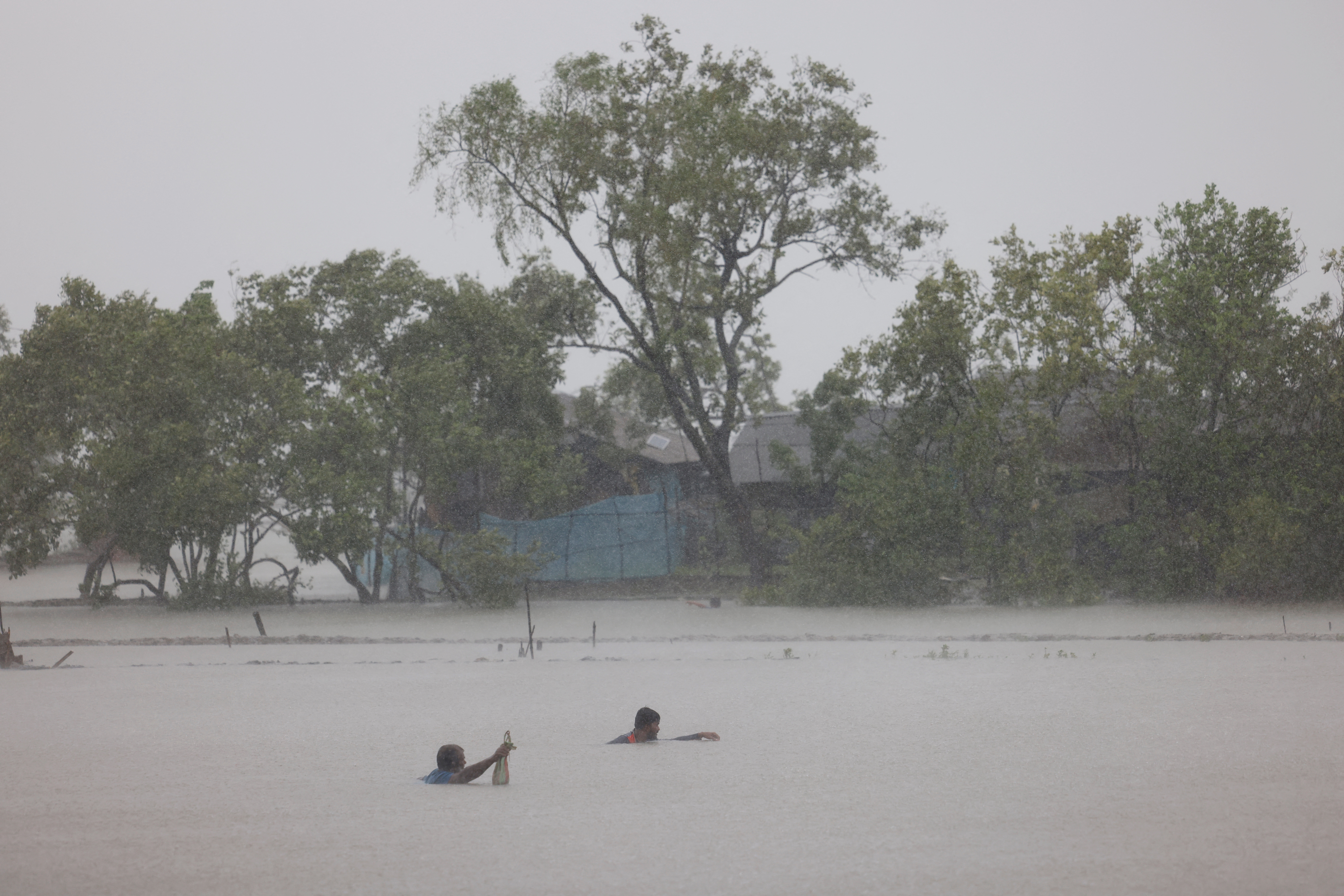 People fish at the shrimp and crab farms that are flooded due to heavy rain, as Cyclone Remal hits the country, in the Shyamnagar area of Satkhira