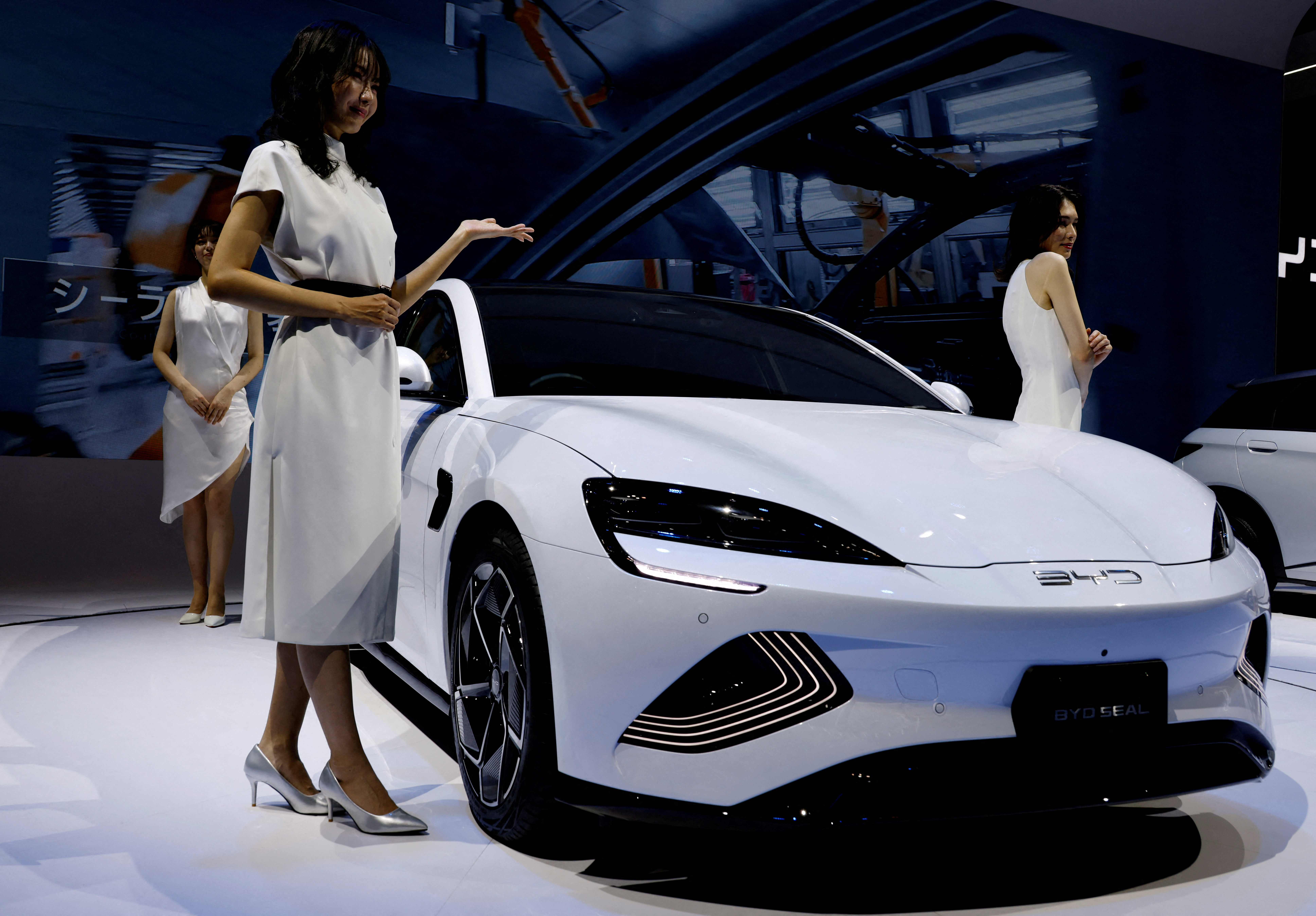 Models pose next to Chinese automobile manufacturer BYD's BYD SEAL during the Japan Mobility Show in Tokyo