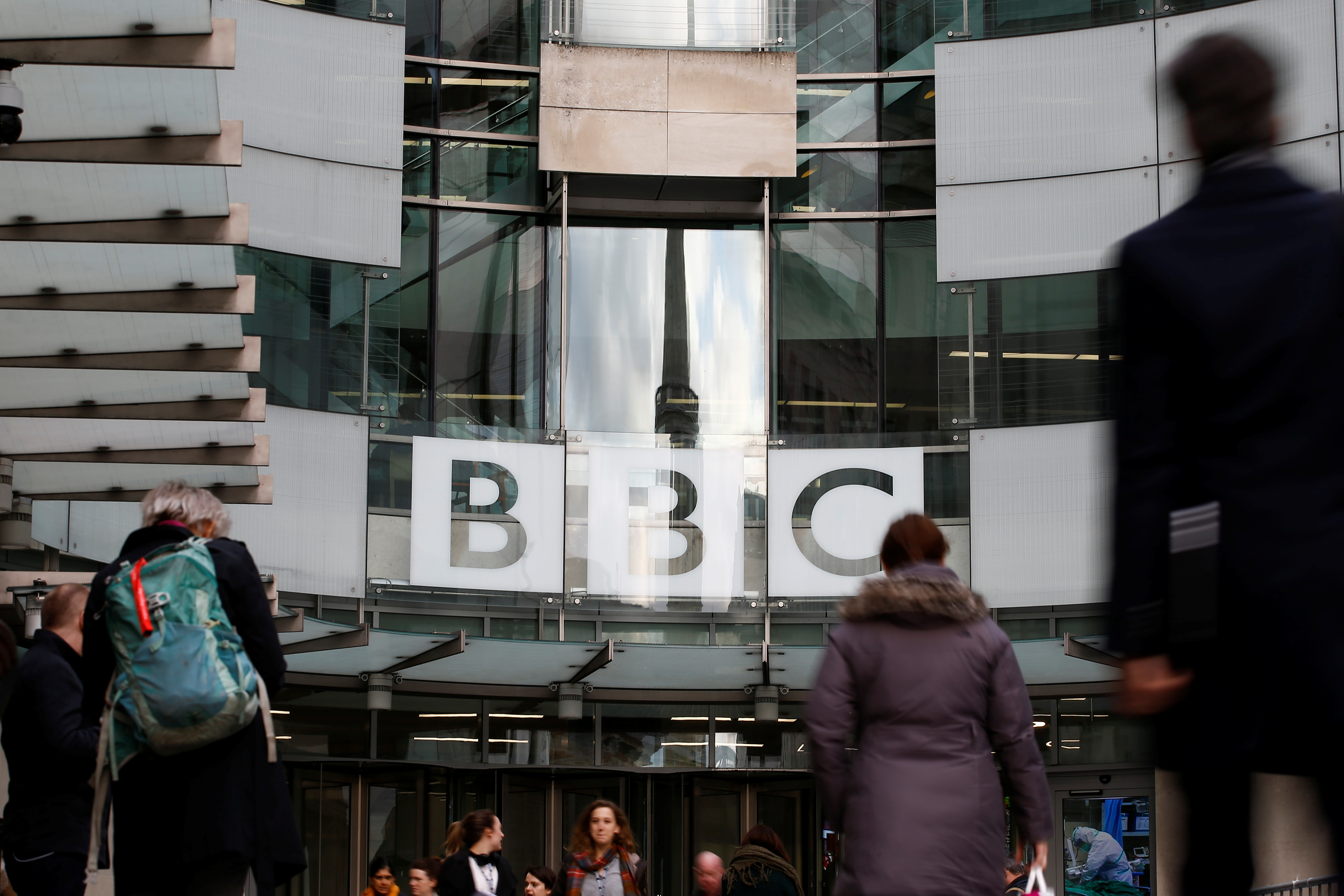 Pedestrians walk past a BBC logo at Broadcasting House, as the corporation announced it will cut around 450 jobs from its news division, in London