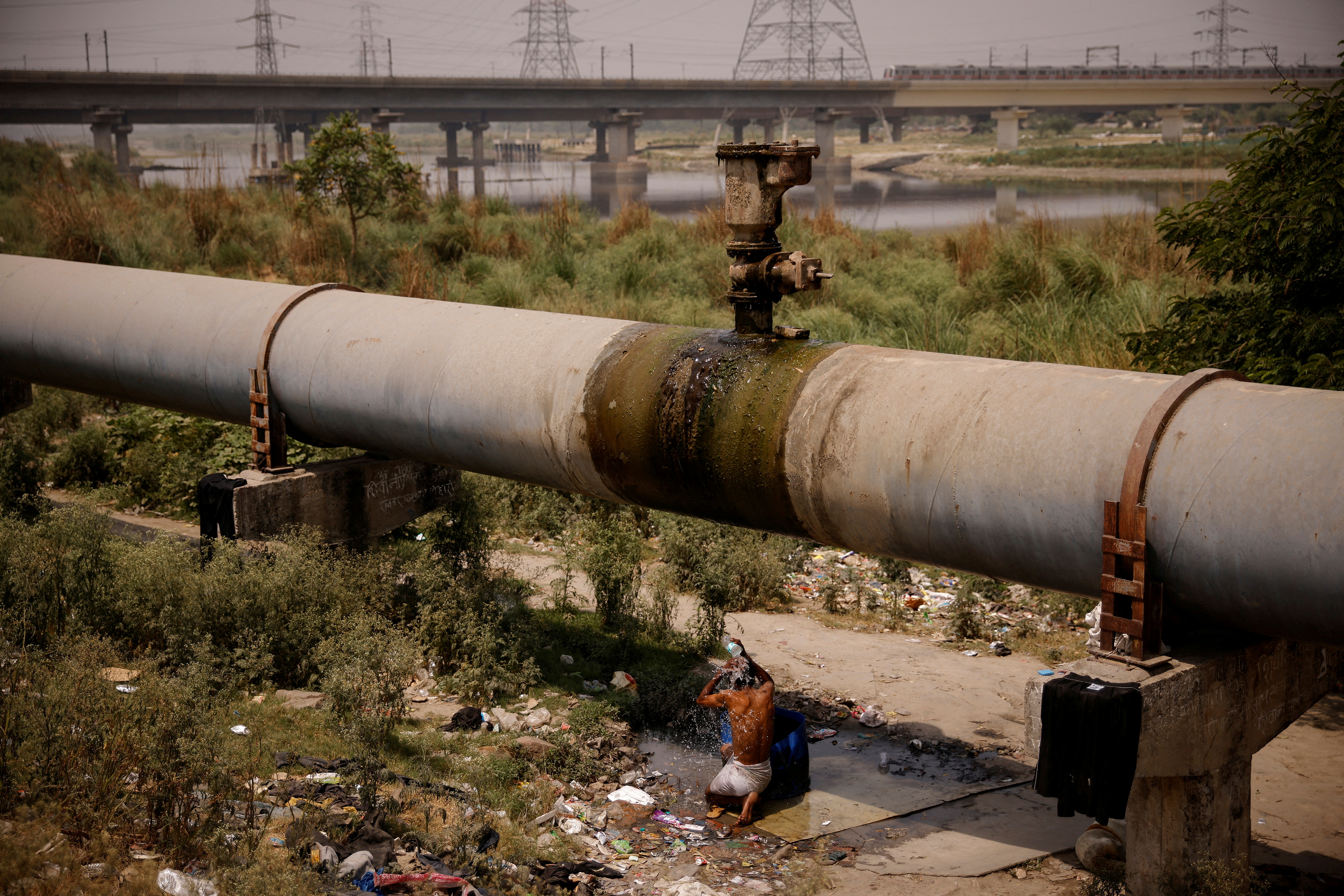 A man bathes under a broken water pipeline on a hot summer day in New Delhi