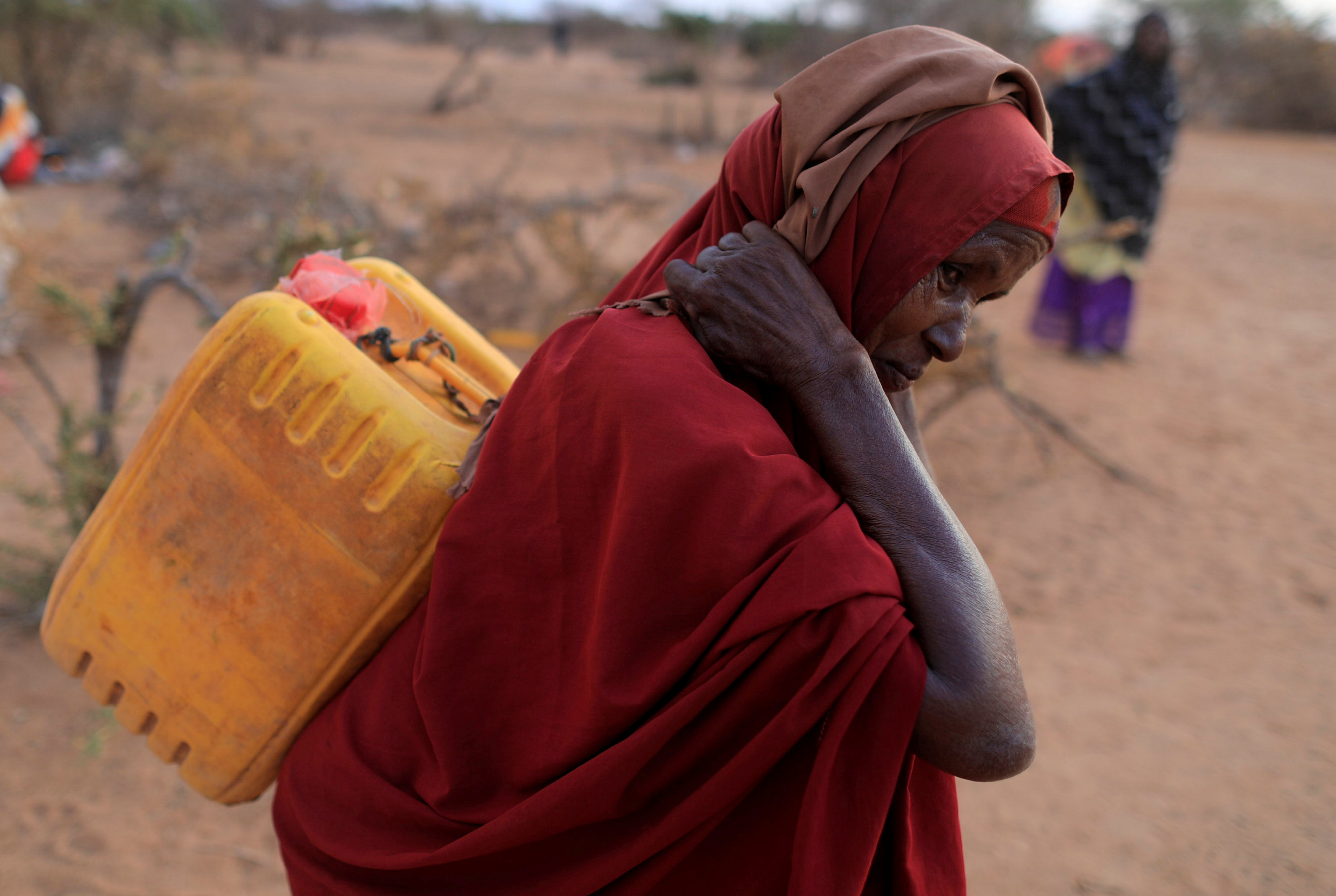 An internally displaced woman from drought hit area carries a jerrycan of water as she walks towards her shelter at a makeshift settlement area in Dollow