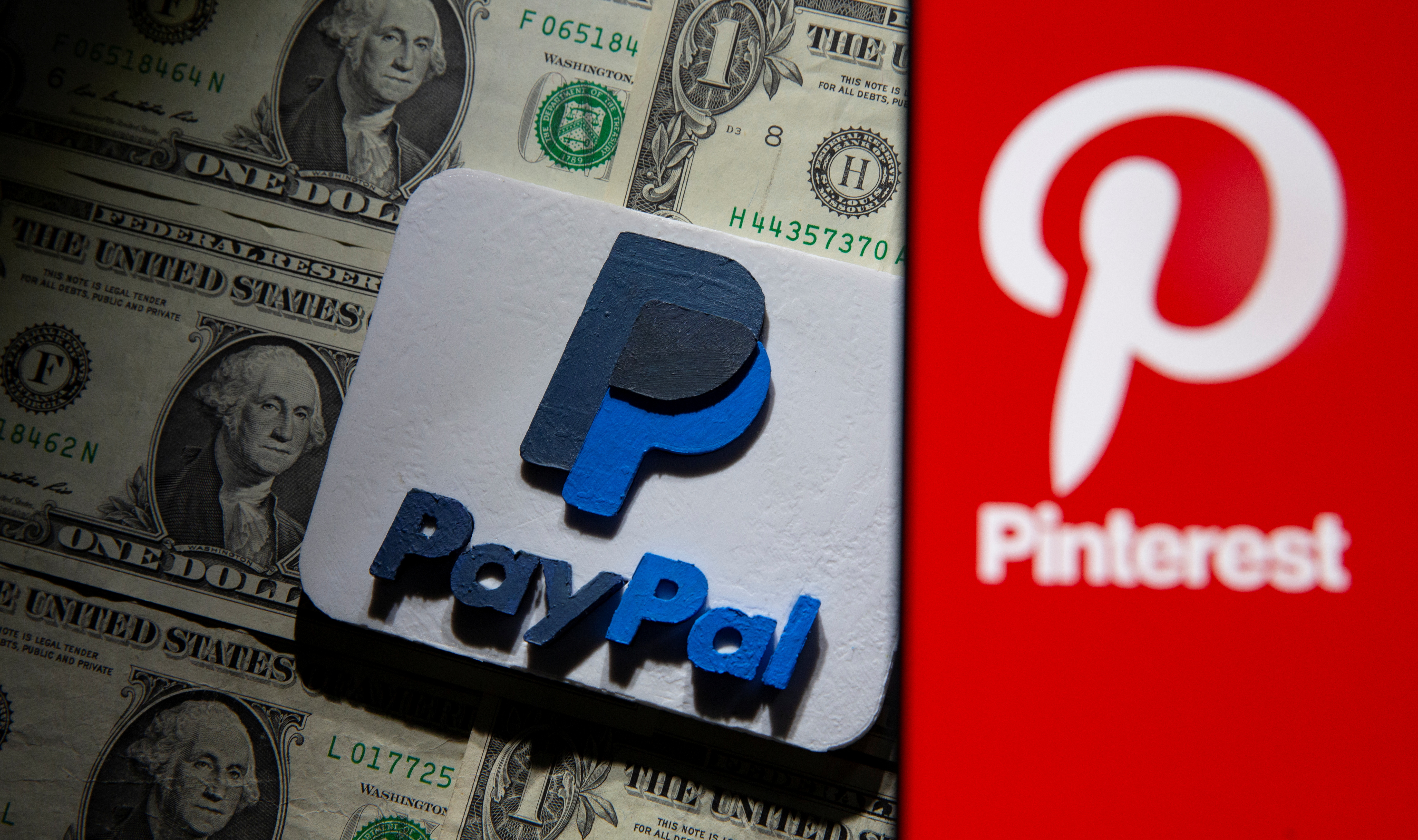 Pinterest logo is seen on smartphone placed over U.S. dollar banknotes and 3D printed PayPal logo in this illustration