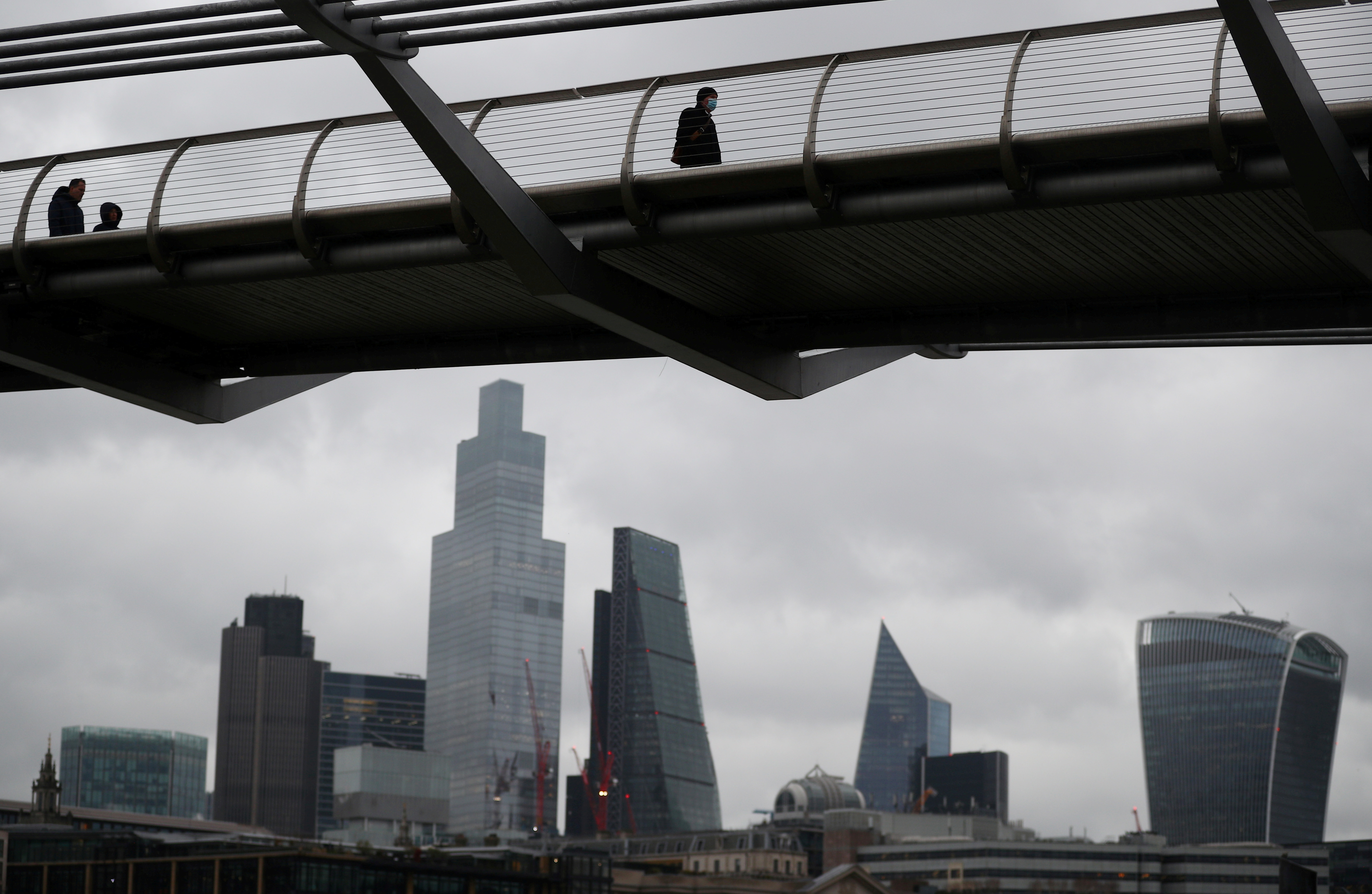 People walk across the Millennium Bridge in London's financial district amid the coronavirus disease (COVID-19) pandemic in London