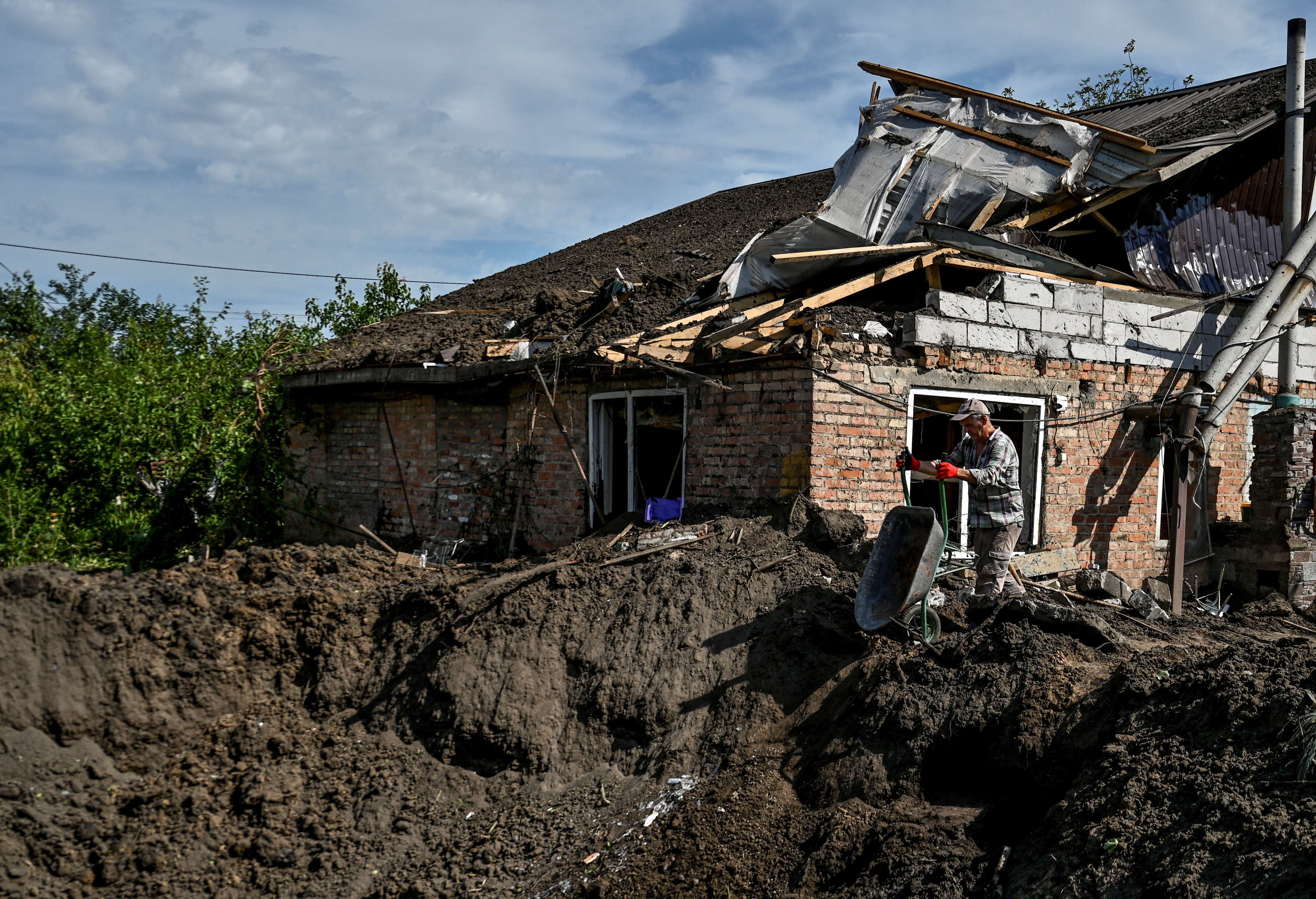 A man throws debris of a residential house into a crater left by a Russian missile strike in the settlement of Kushuhum