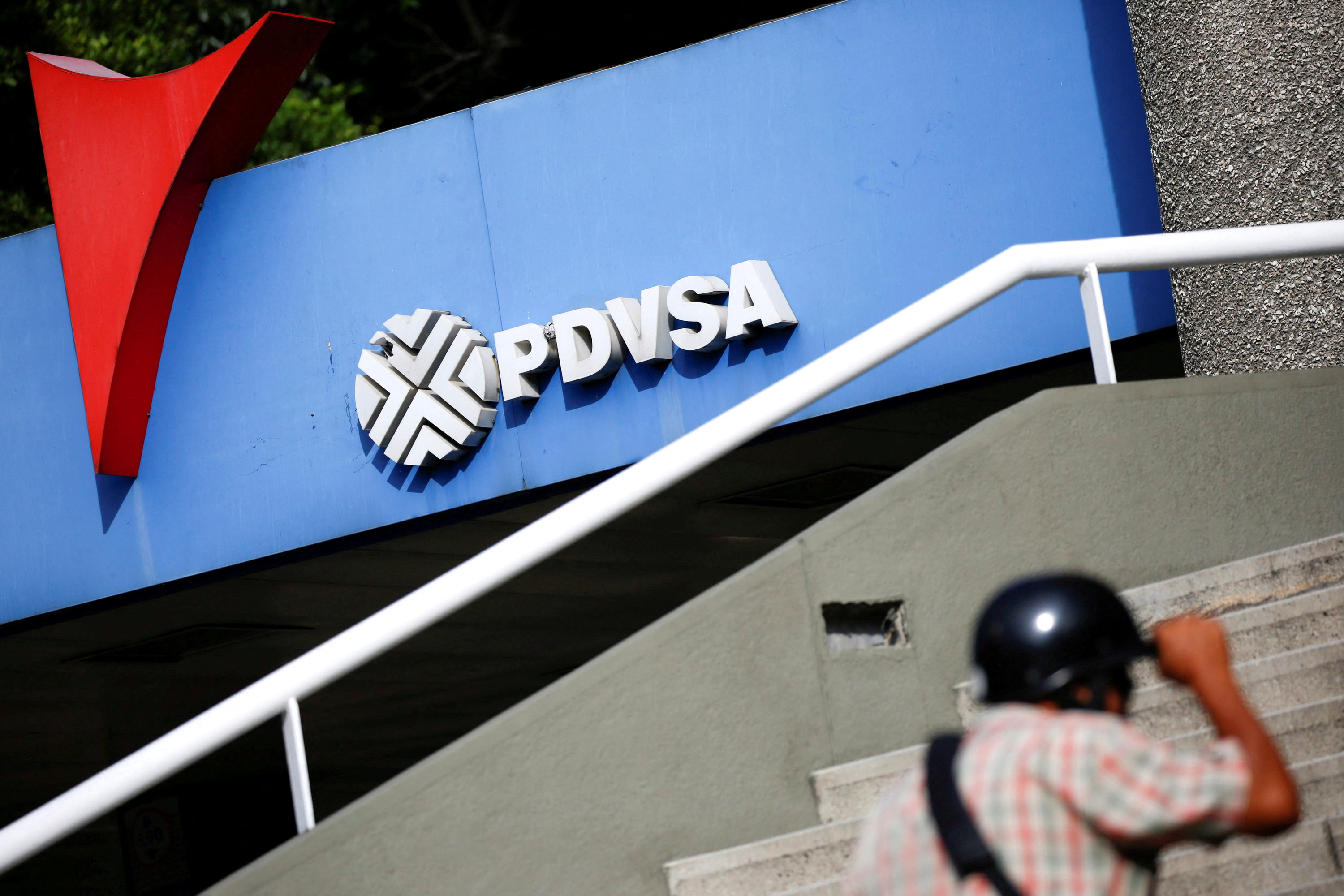 A man walks past a gas station with the logo of the Venezuelan state oil company PDVSA in Caracas
