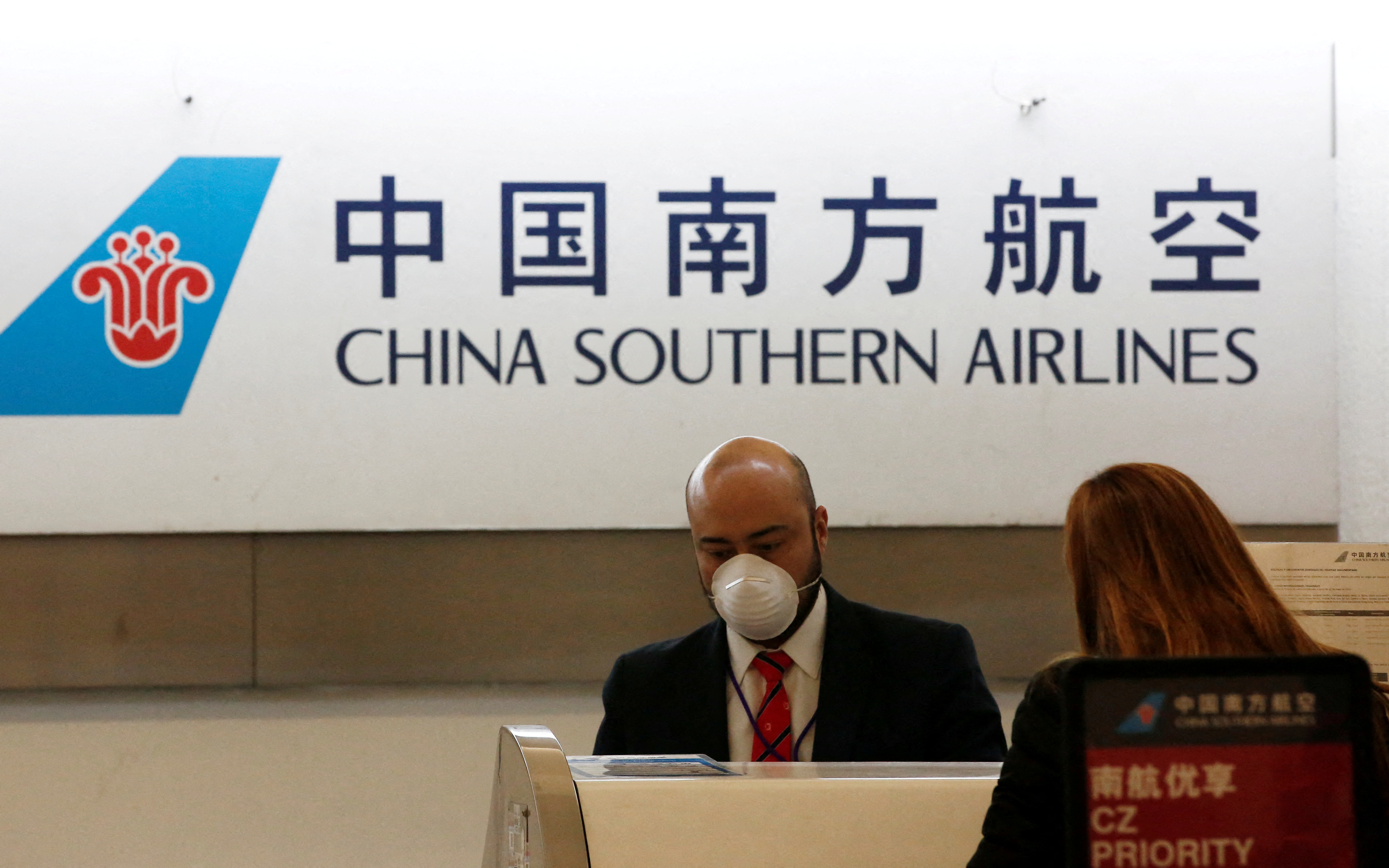 A China Southern Airlines employee wears a surgical mask as a preventive measure in light of the coronavirus outbreak in China, while he attends a customer behind the counter at Benito Juarez international airport in Mexico City