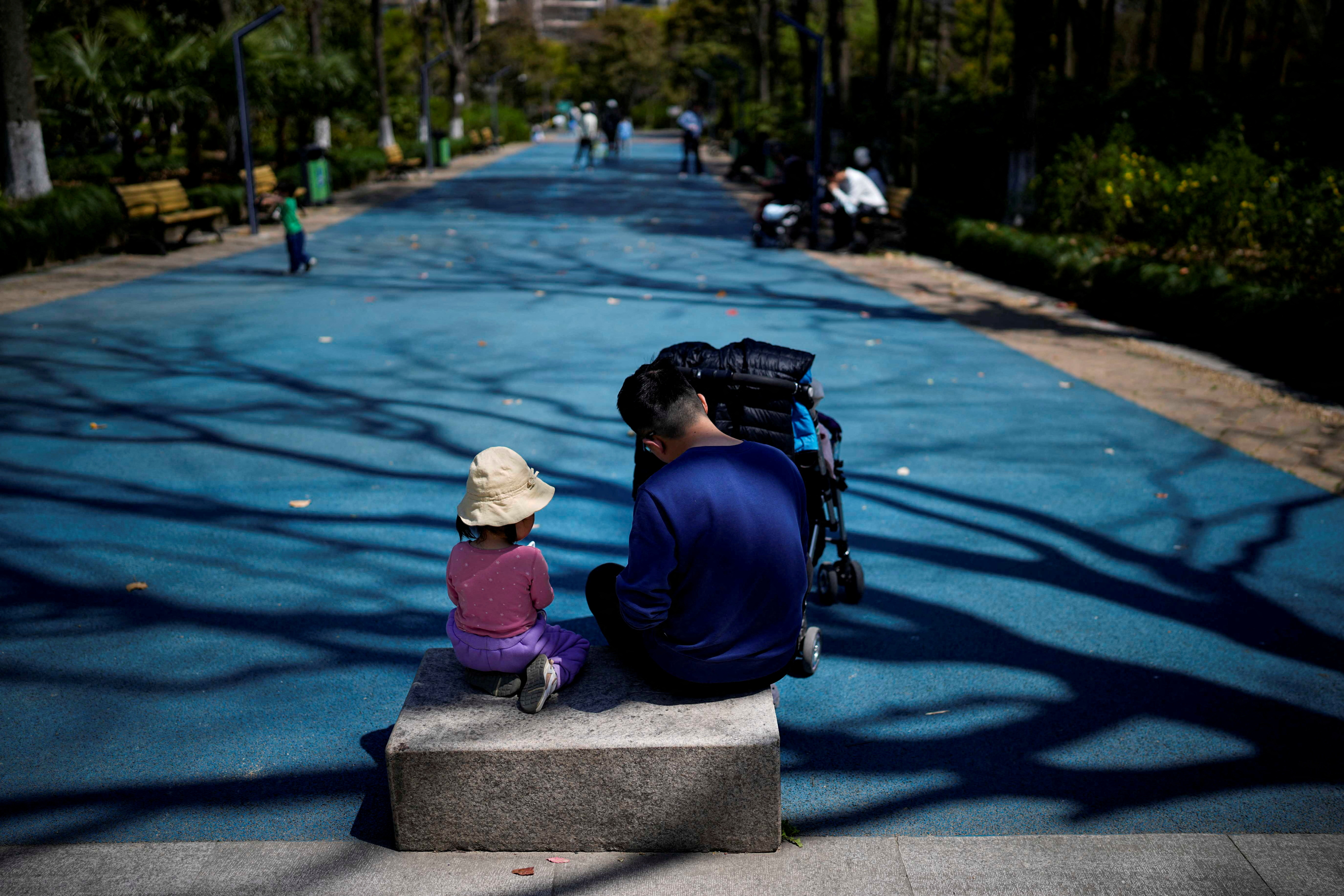 A little girl sits with her dad in a park in Shanghai